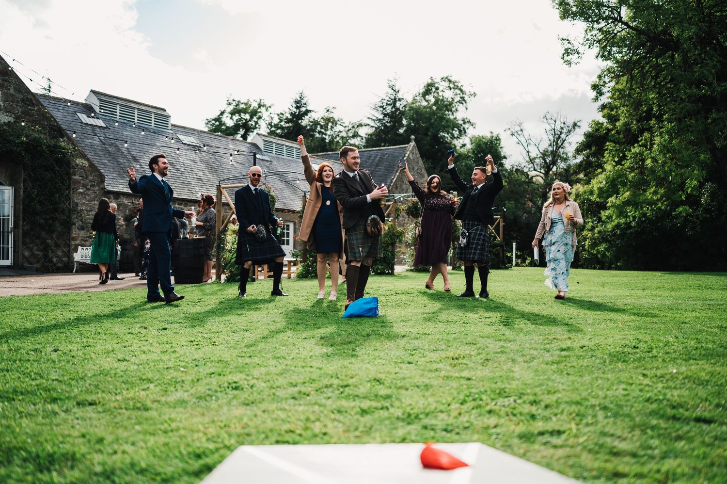 Wedding guests playing lawn games and socializing outdoors on a grassy area during a summer celebration.