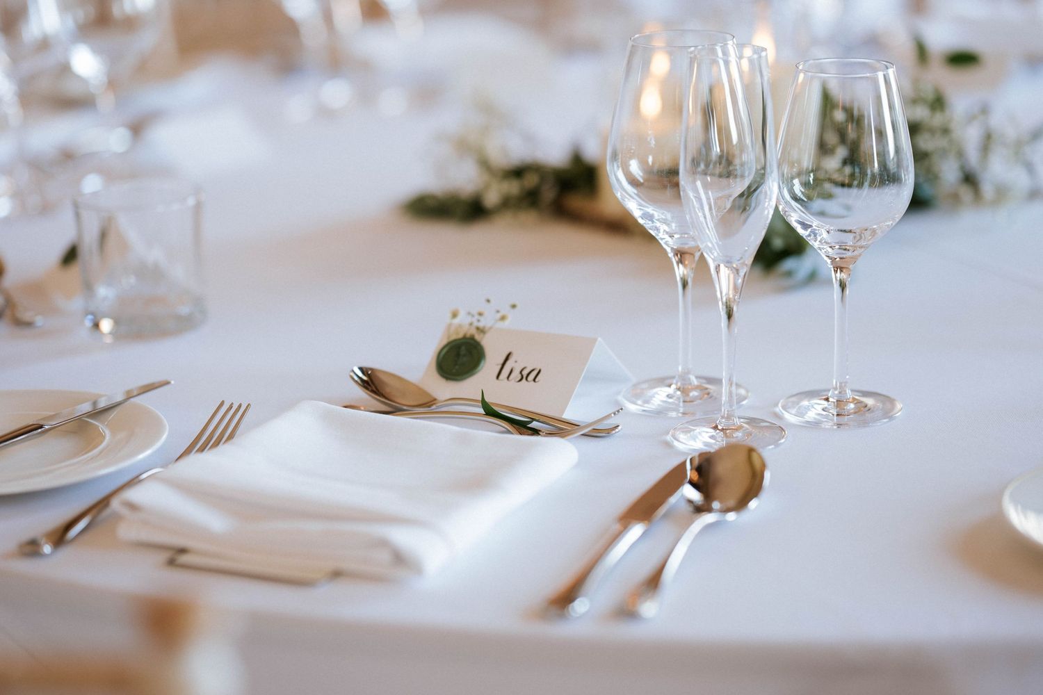 Elegant table settings with wine glasses and white linens at a formal event.