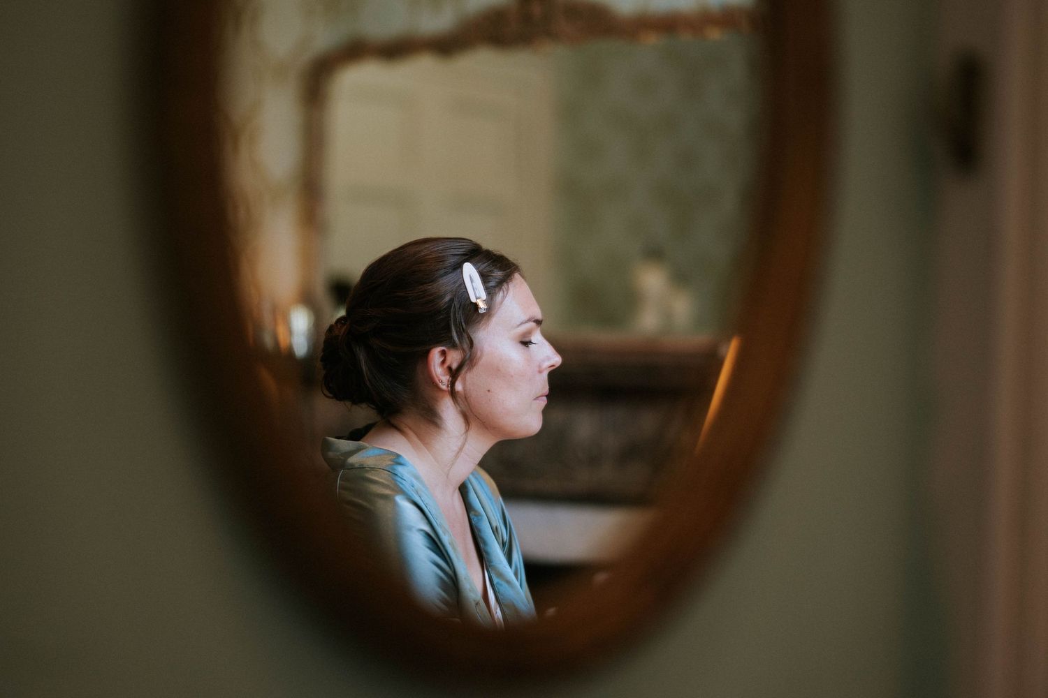 Reflection of a person in a vintage oval mirror during wedding day preparations.
