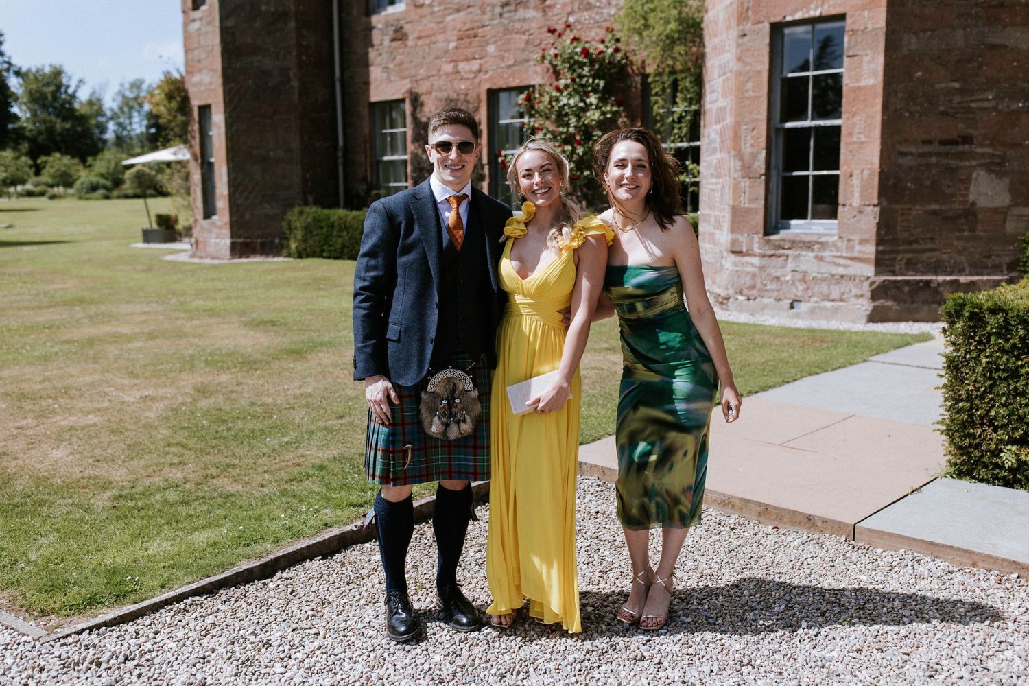 Wedding guests gather outside rustic brick venue on sunny afternoon.