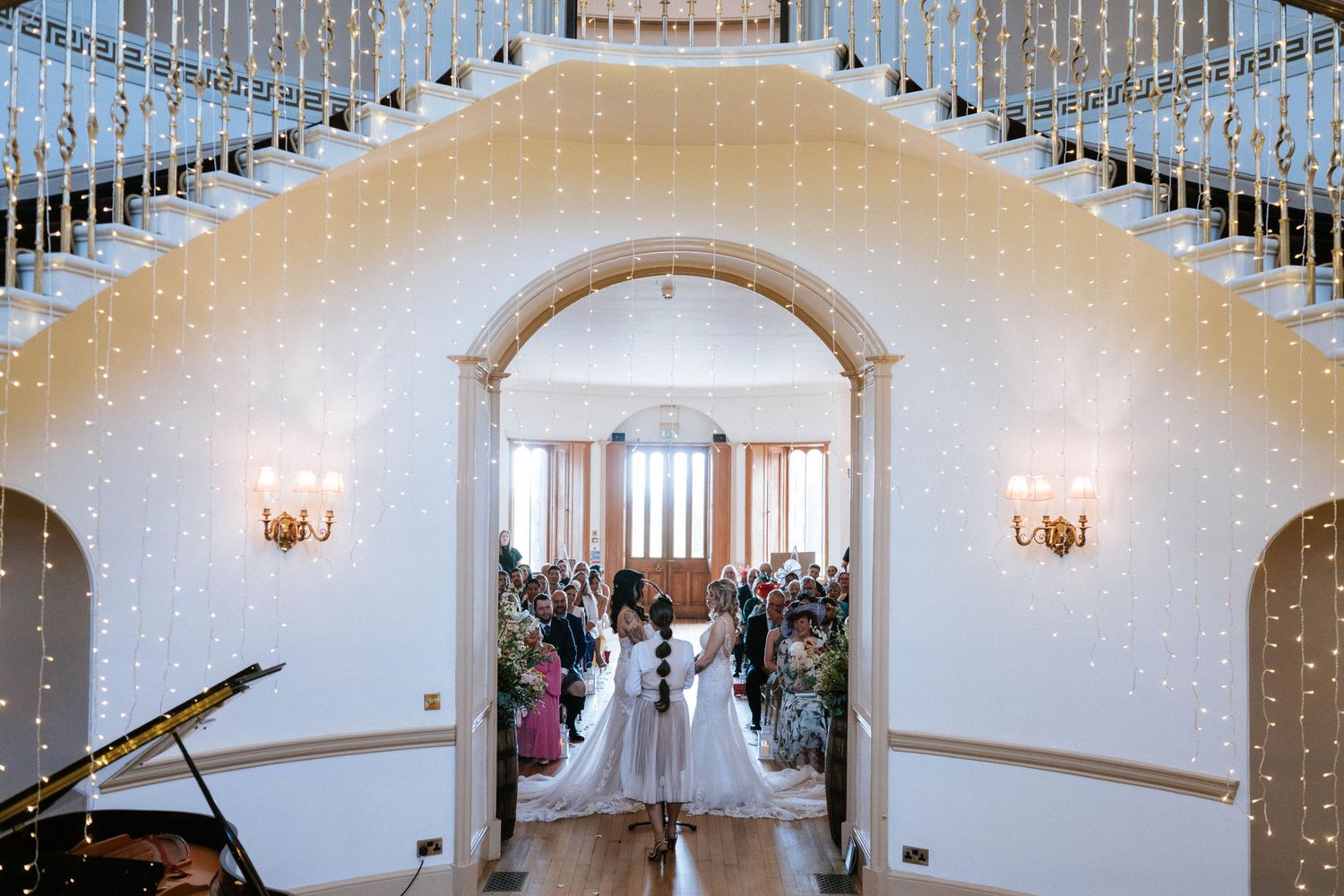 Grand staircase decorated with string lights leads to wedding ceremony space with seated guests.