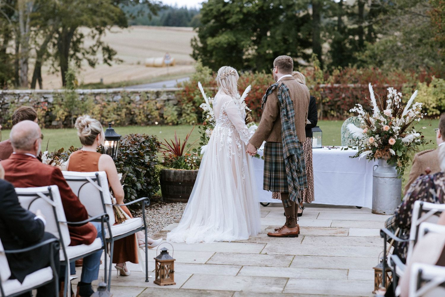 Outdoor wedding ceremony with traditional Scottish attire and floral decorations.