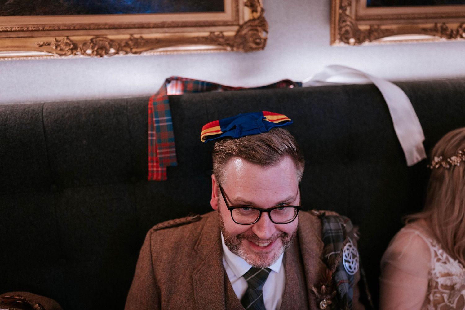 A guest wearing a brown suit and novelty hat smiles during wedding festivities.