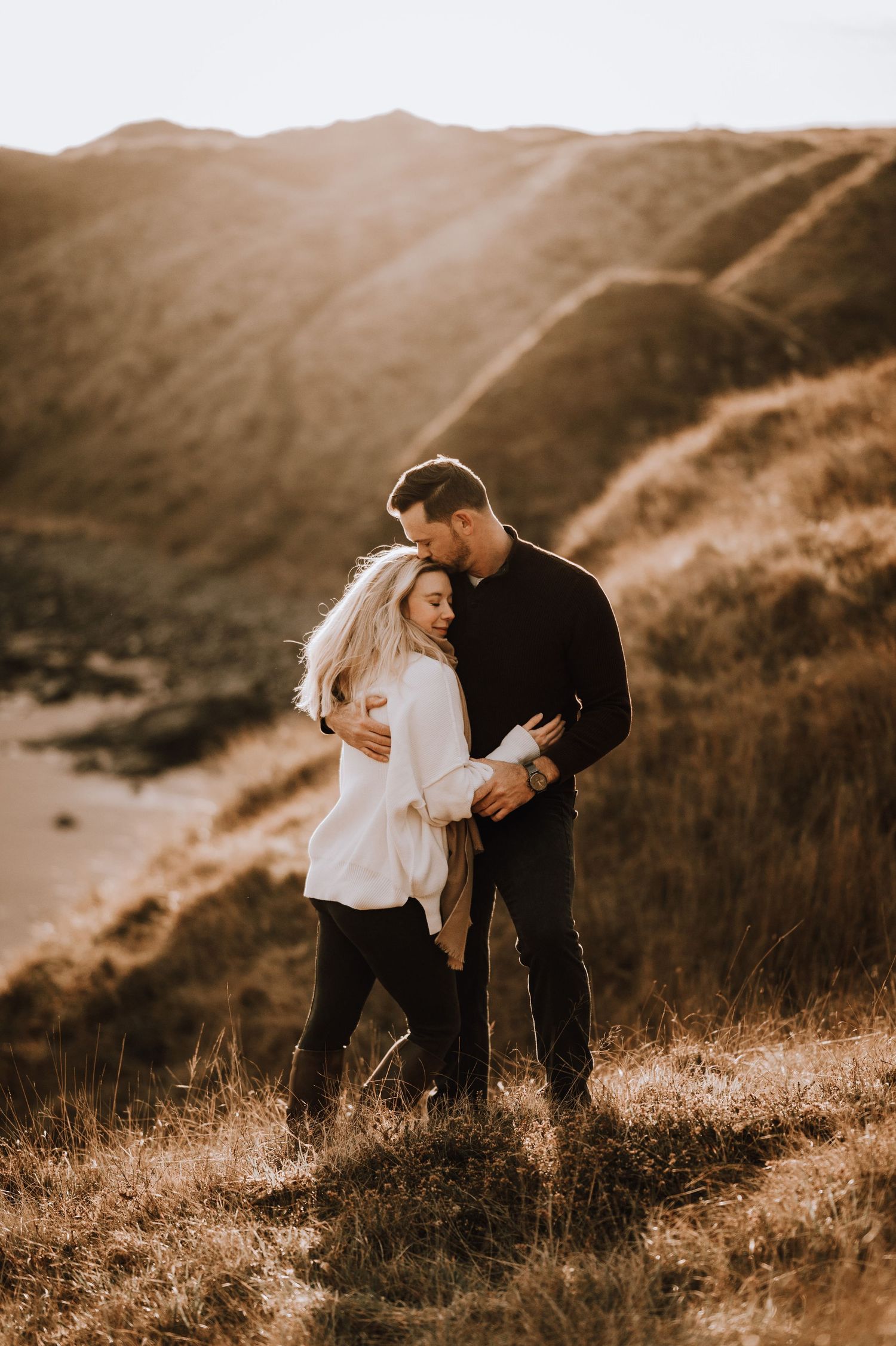 Engagement photography session Aberdeen. A couple shares playful moments on a golden hillside during sunset.