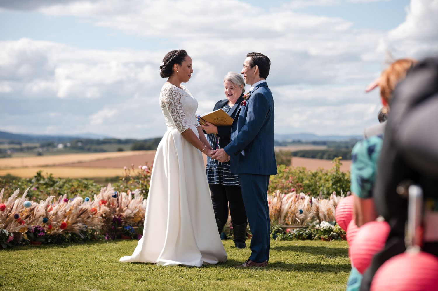 Wedding ceremony taking place in front of a scenic rural landscape with rolling hills.