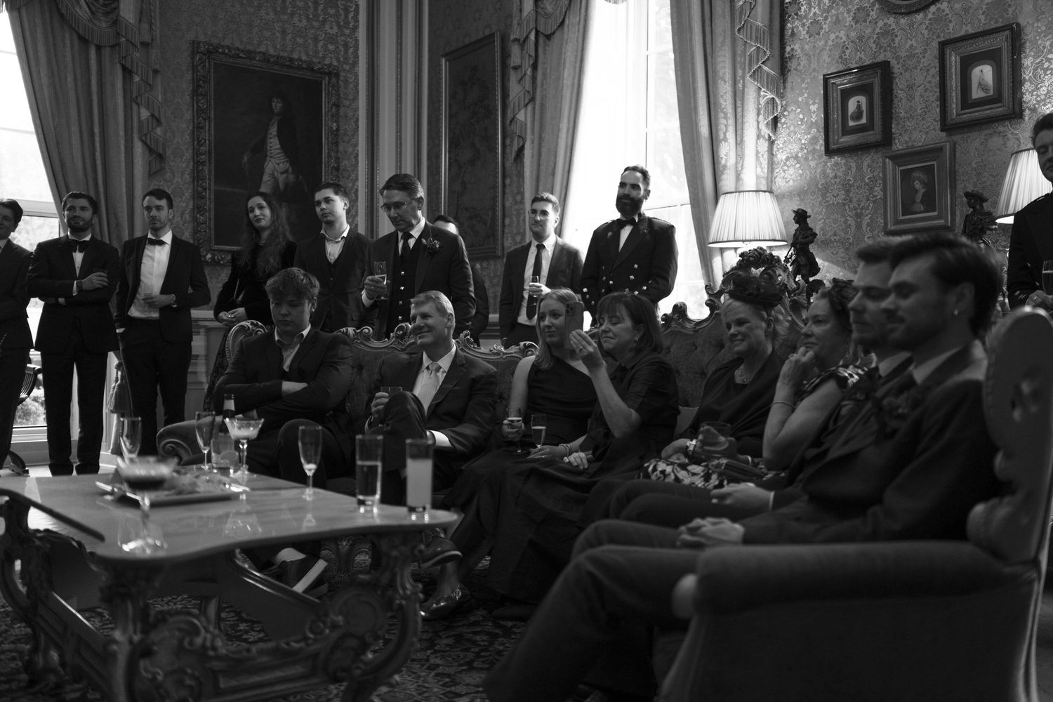 Wide view of guests seated in an ornate room with gilded walls and large windows.