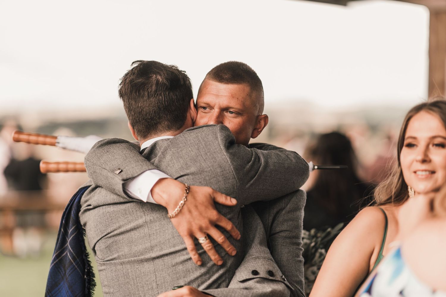 Wedding guests share emotional hugs during an outdoor celebration.