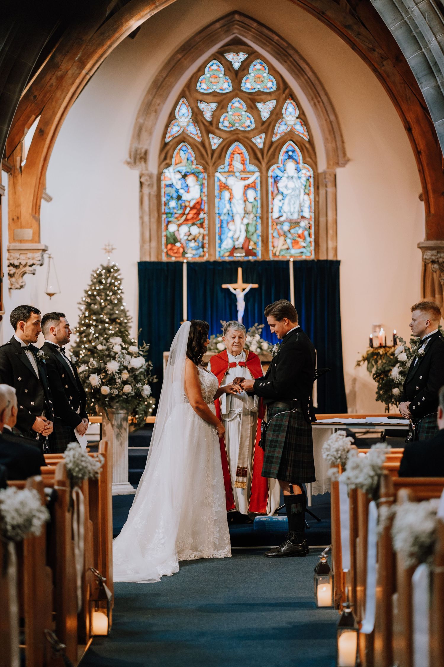 A wedding ceremony in progress beneath Gothic stained glass windows with Christmas decorations.