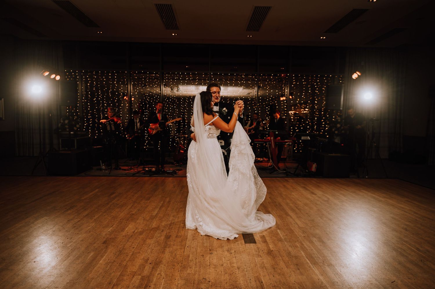 Couple shares intimate first dance moment on wooden dance floor with sparkly backdrop.