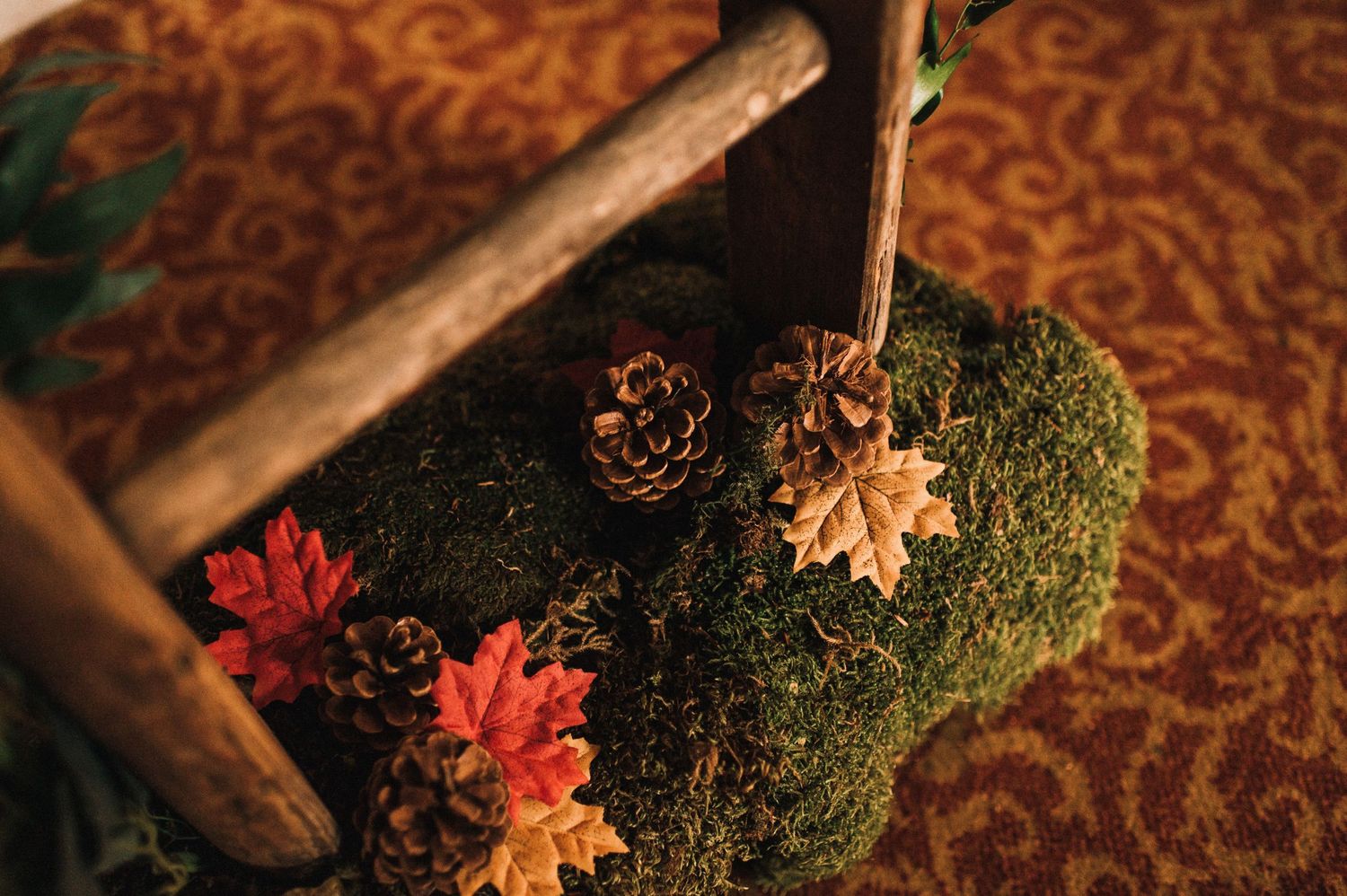 Autumn-themed decor with moss, pinecones, and red maple leaves on patterned carpet.