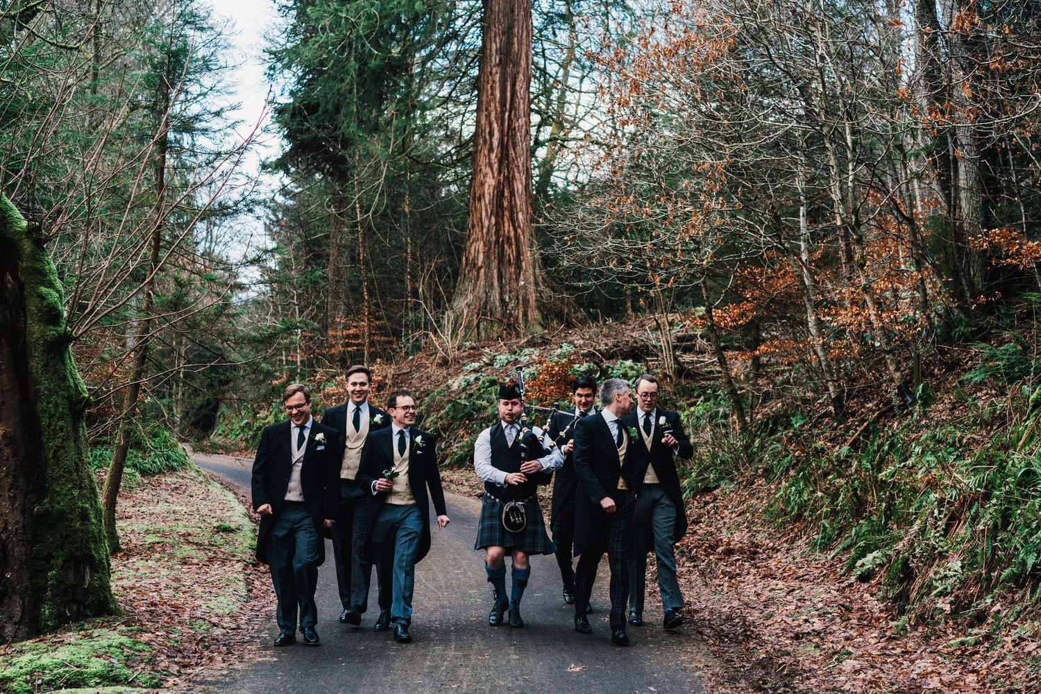 Groomsmen walking together along a forest path wearing formal attire.
