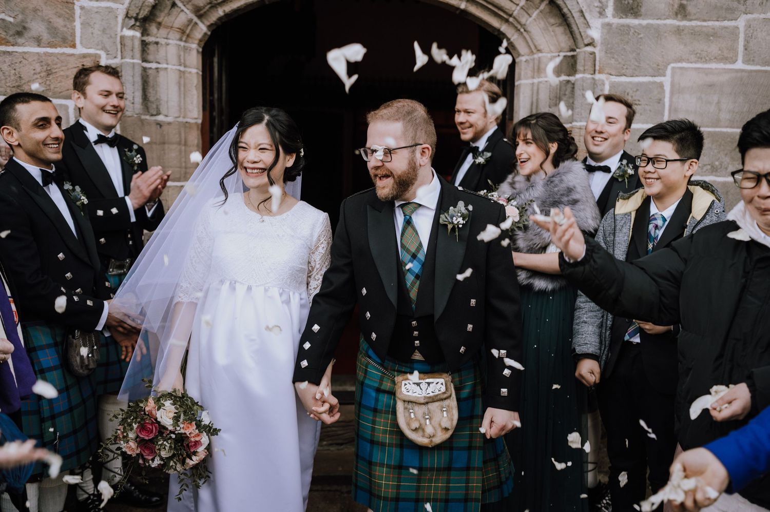 Newlyweds exit church under shower of confetti with Scottish kilt traditions.