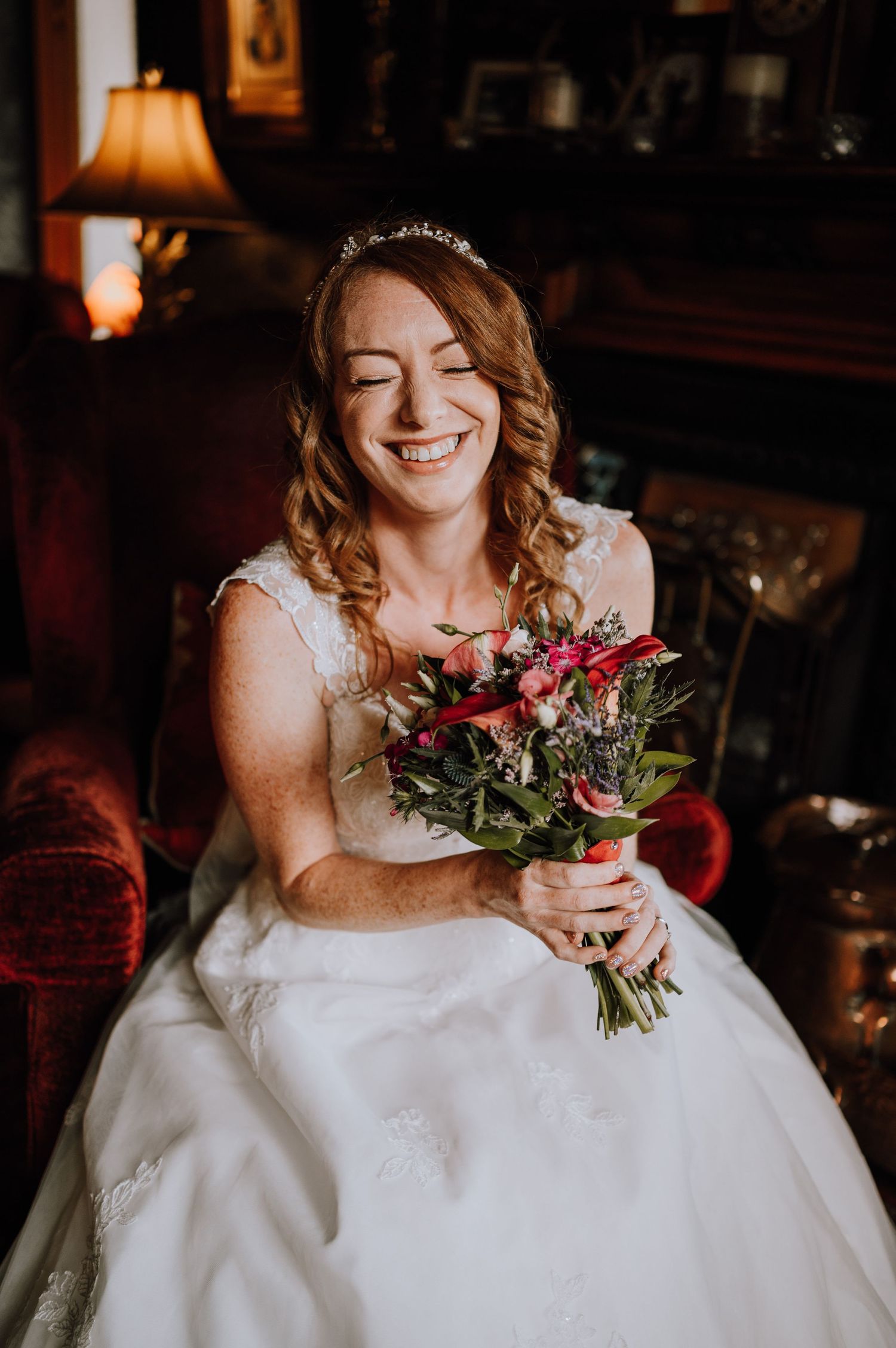 Bride in white gown smiling with pink bouquet in warm-lit room.