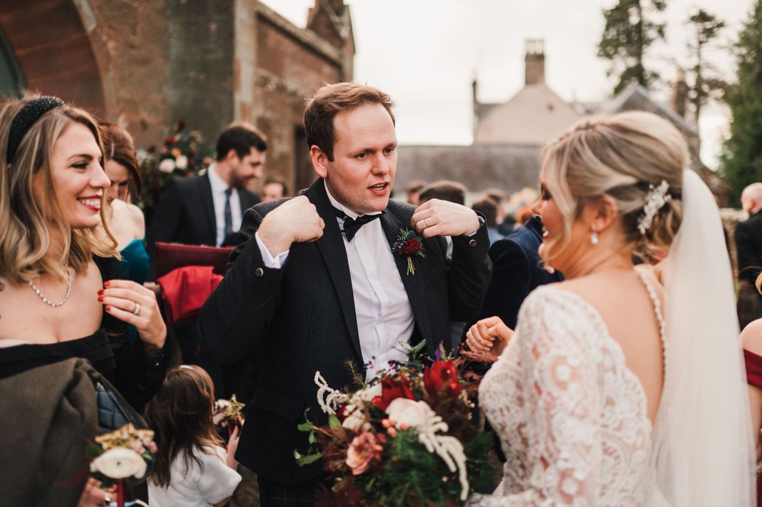 Wedding party celebrates outside traditional brick church during winter ceremony.