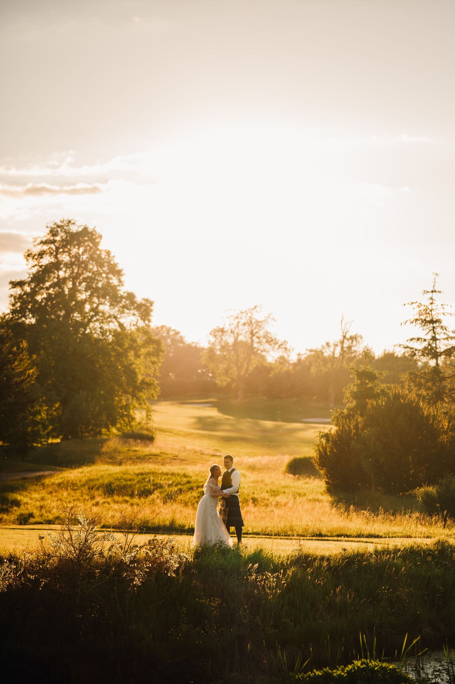 A wedding couple silhouetted against a golden sunset on a golf course with trees in the background.