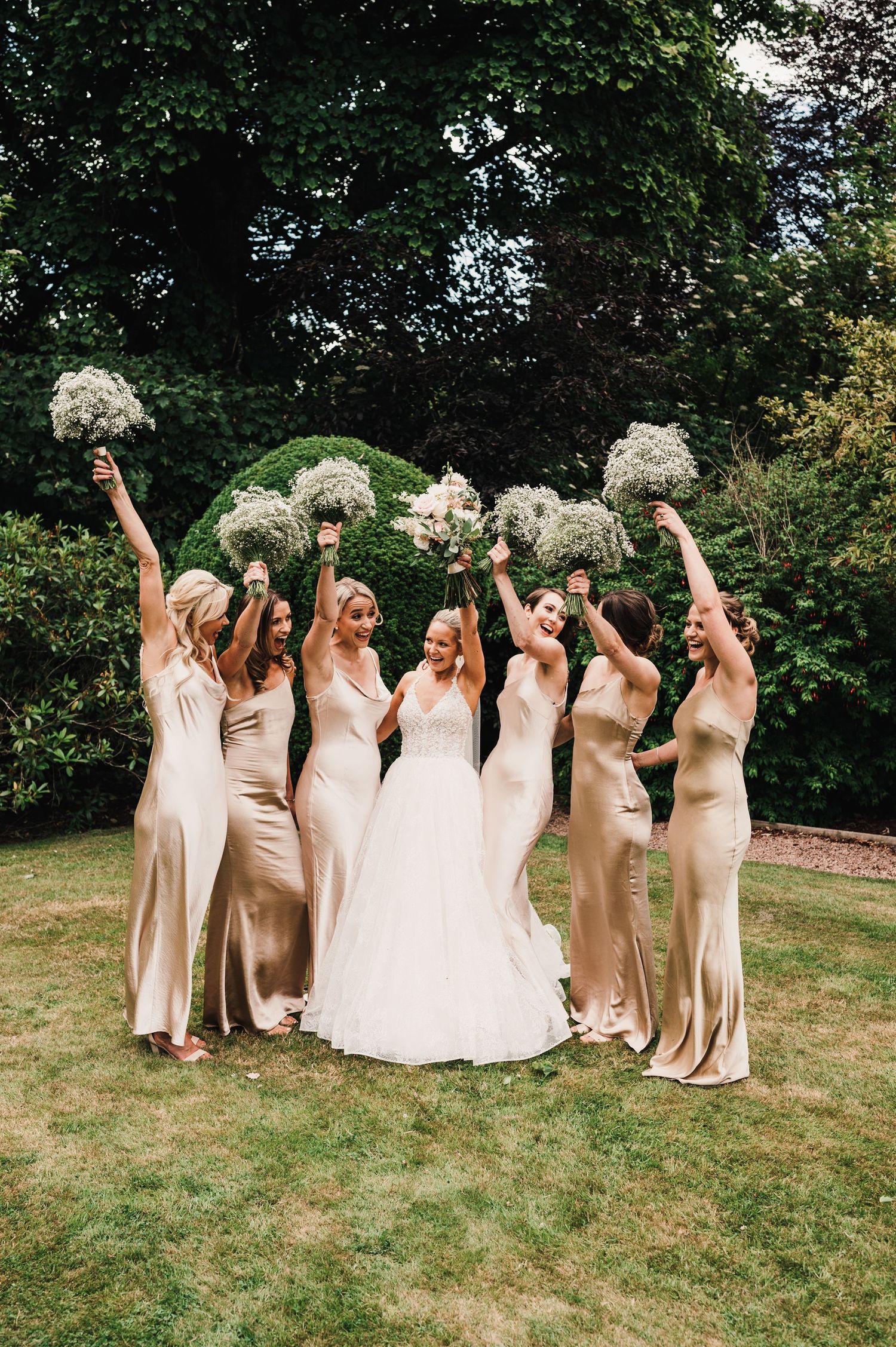 Wedding party with groomsmen in traditional Scottish kilts and bridesmaids in gold dresses pose on lawn.