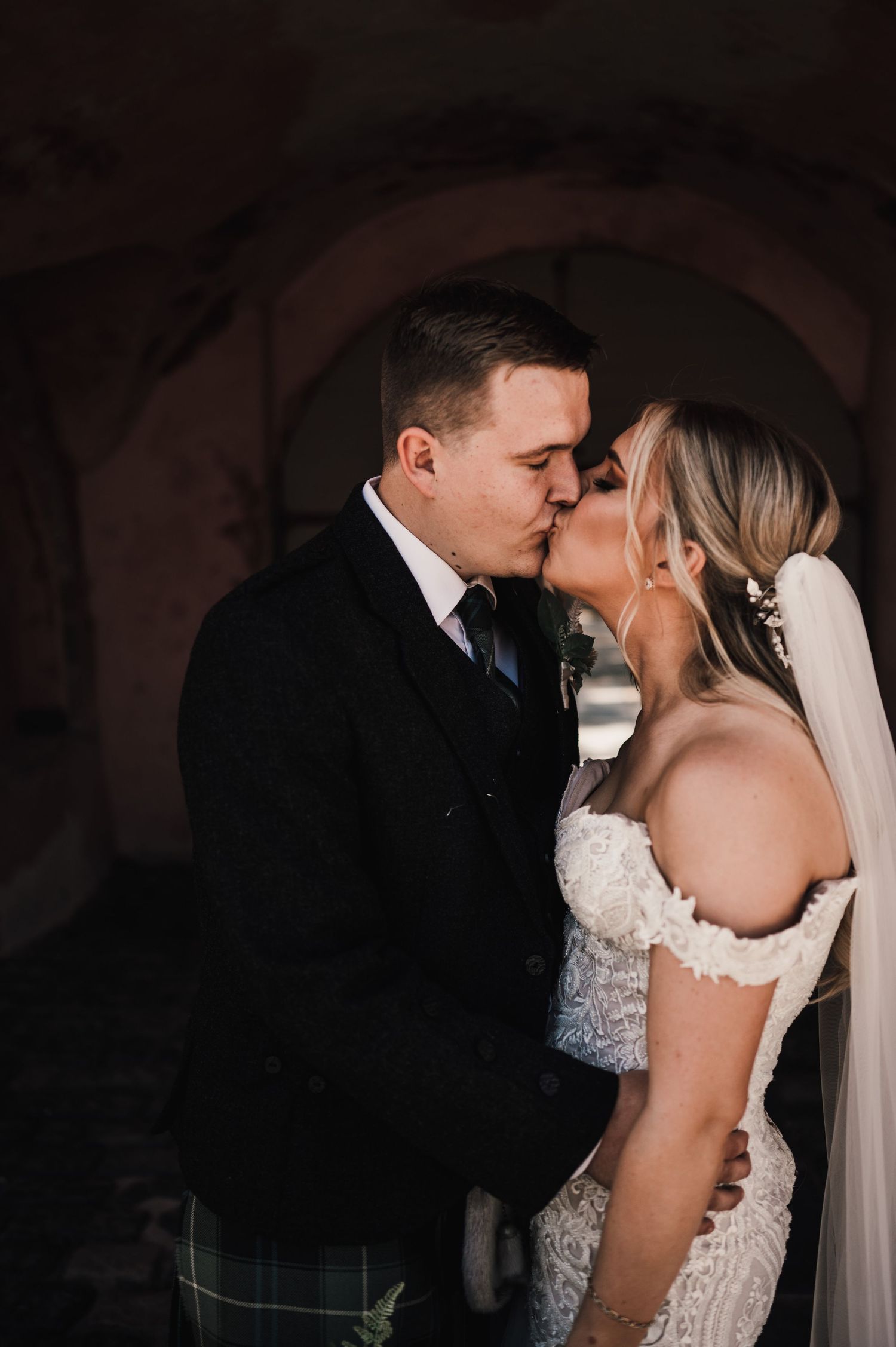An intimate wedding moment captured under an arched doorway with moody lighting.