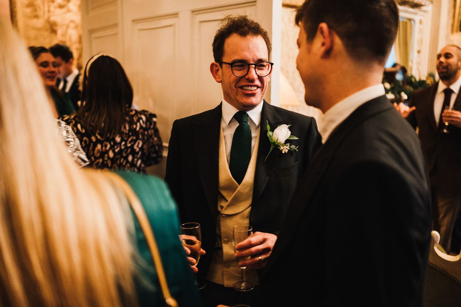Guests enjoying drinks and conversation at an elegant indoor reception with white walls and formal attire.