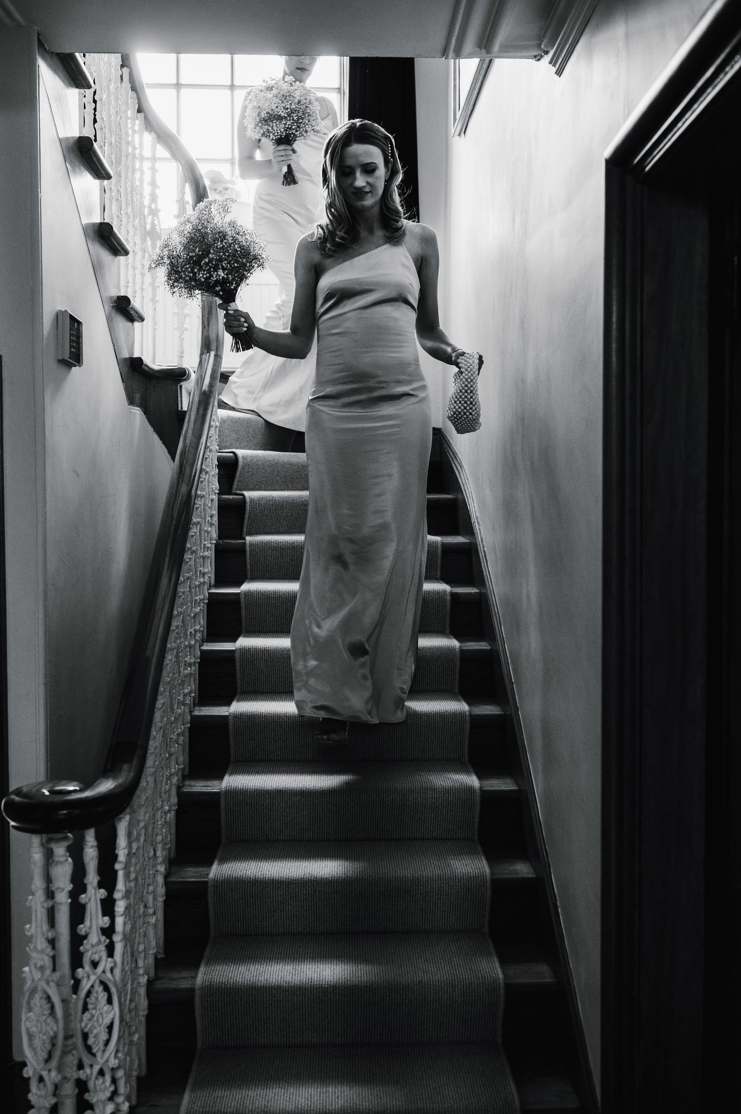Black and white photo of bride in fitted dress posing on vintage staircase.