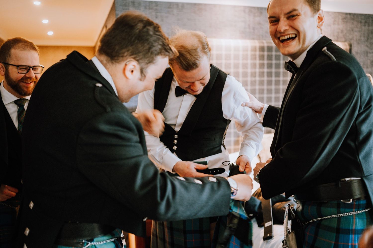 A group preparing for a formal event, wearing kilts and formal attire while sharing laughs.