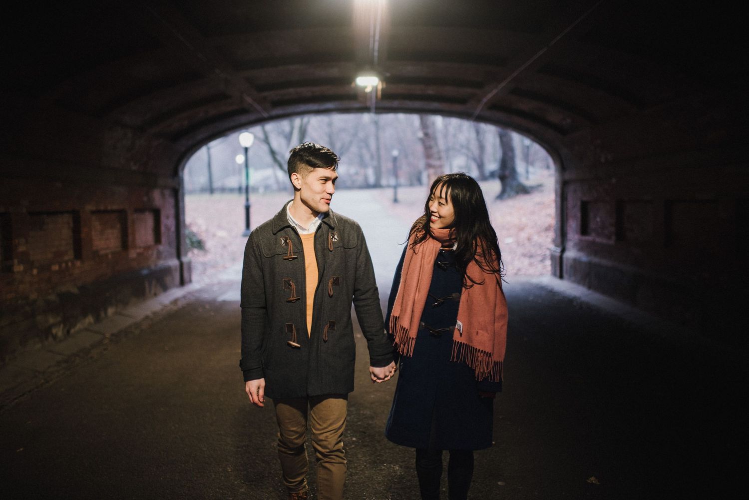 A couple stands in silhouette under a tunnel with bright light in the background.