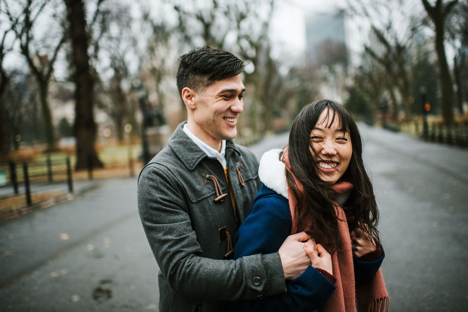 A couple shares a candid laughing moment together on a winter path in Central Park.