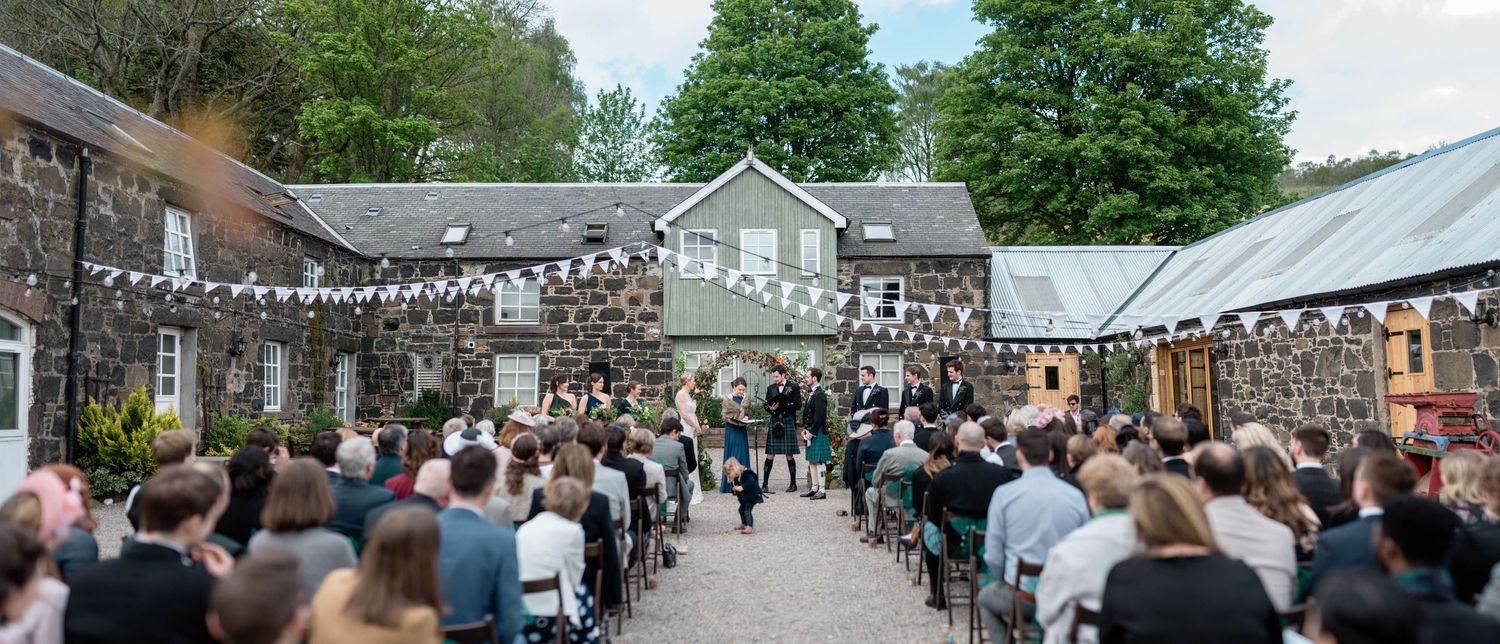 An outdoor wedding ceremony venue with string lights and rows of chairs filled with guests.