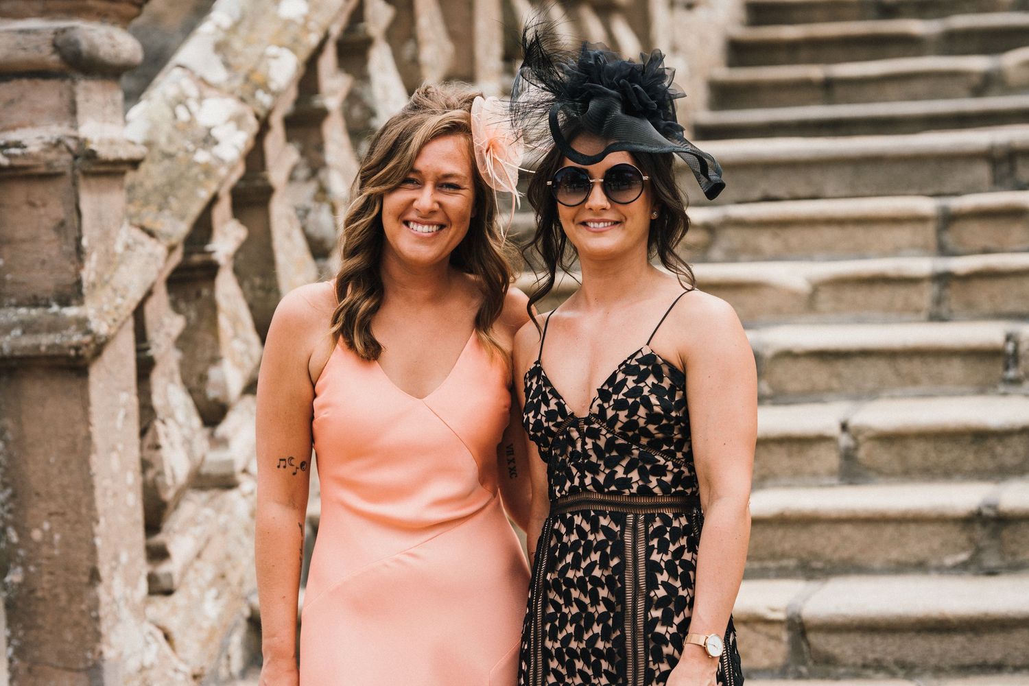 Two wedding guests in formal attire pose together on historic stone staircase.