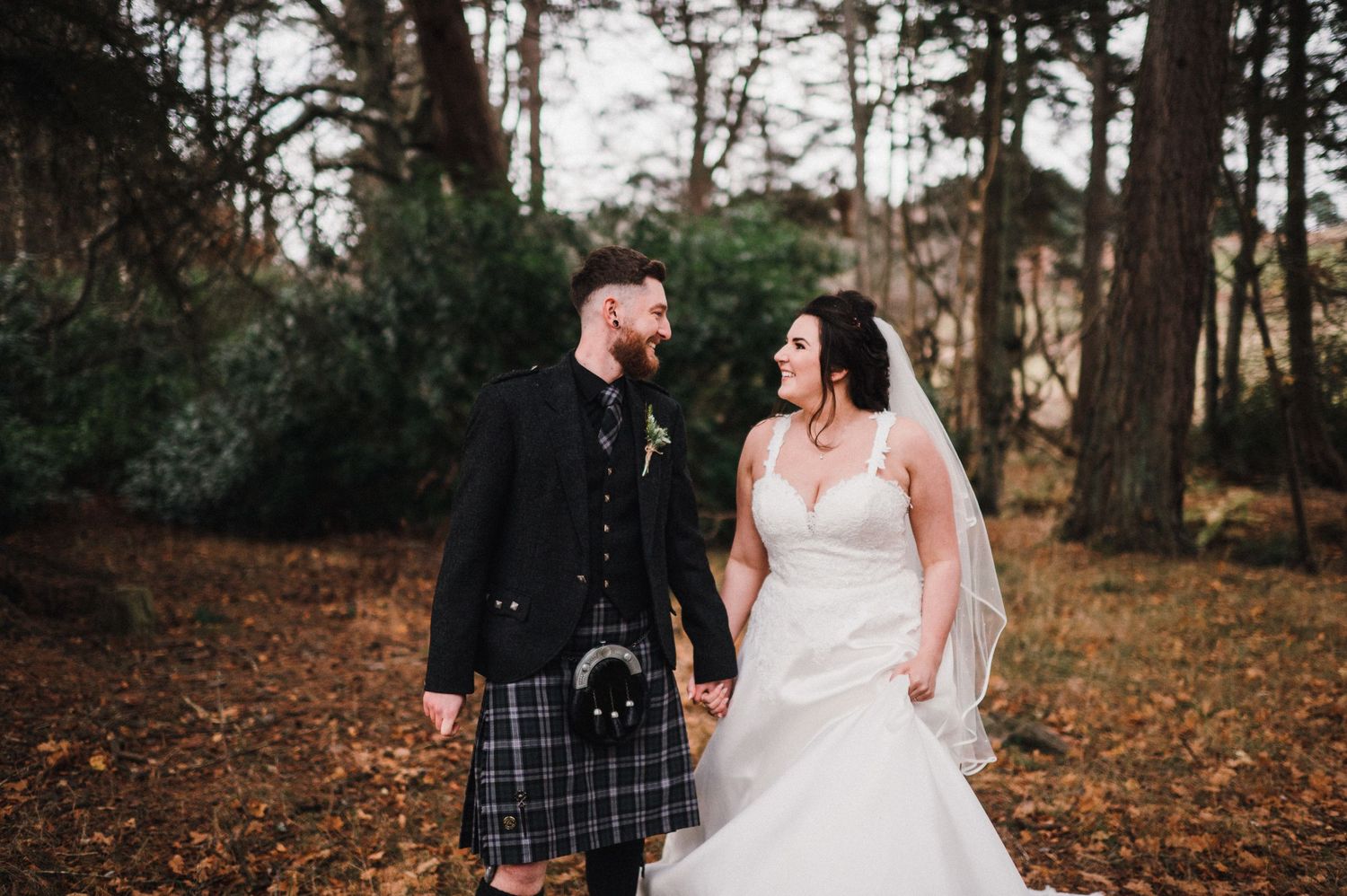 A couple shares a joyful moment in their wedding attire against a backdrop of autumn trees.