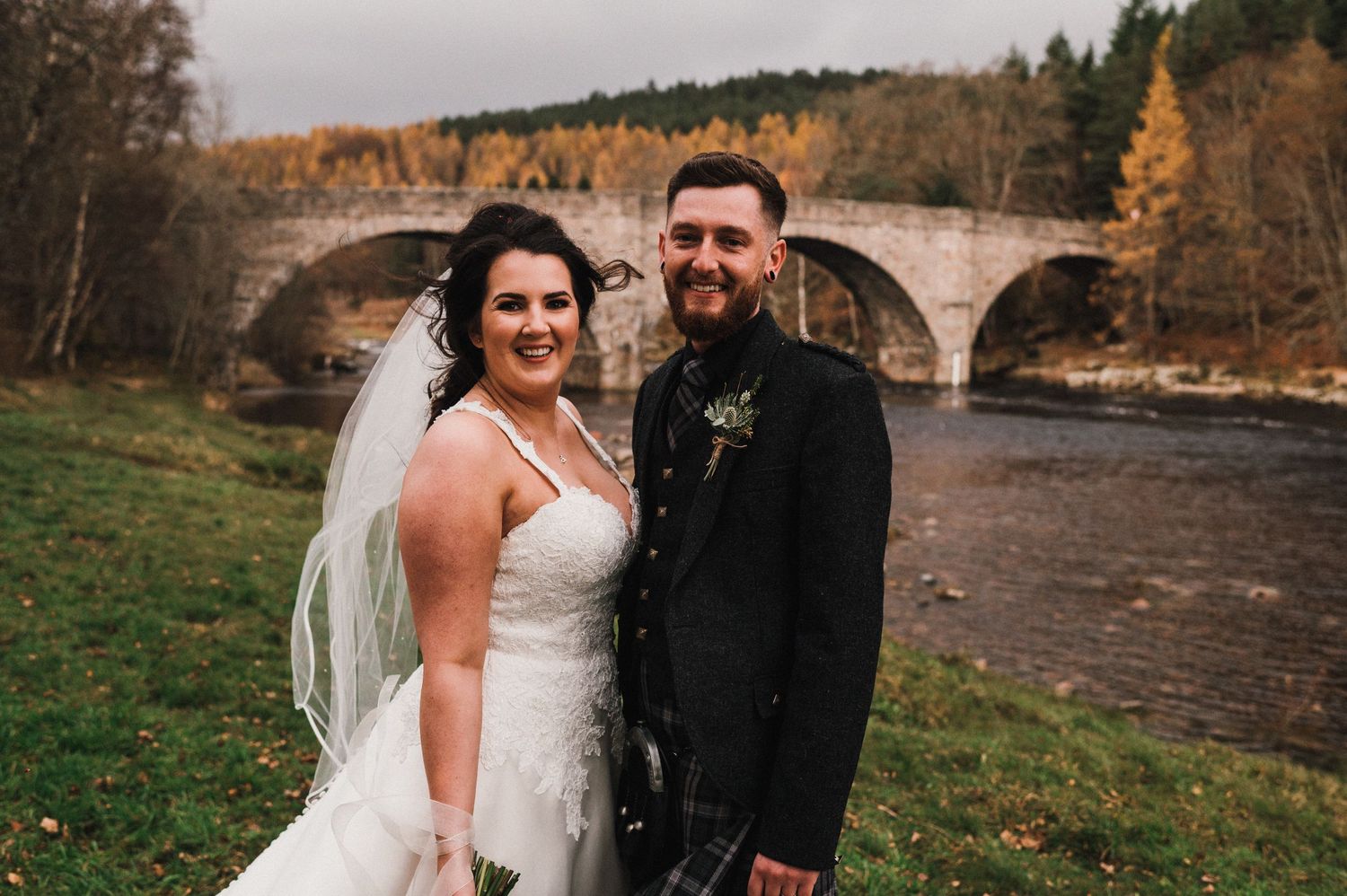 A romantic wedding couple poses in front of a scenic stone bridge during autumn.