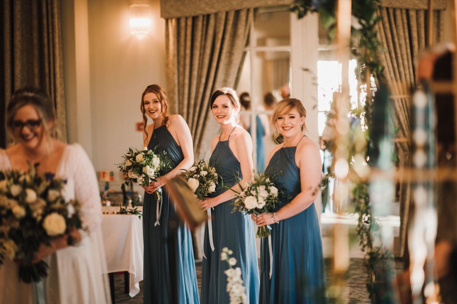 Wedding party in teal blue dresses holding elegant white and cream flower bouquets.