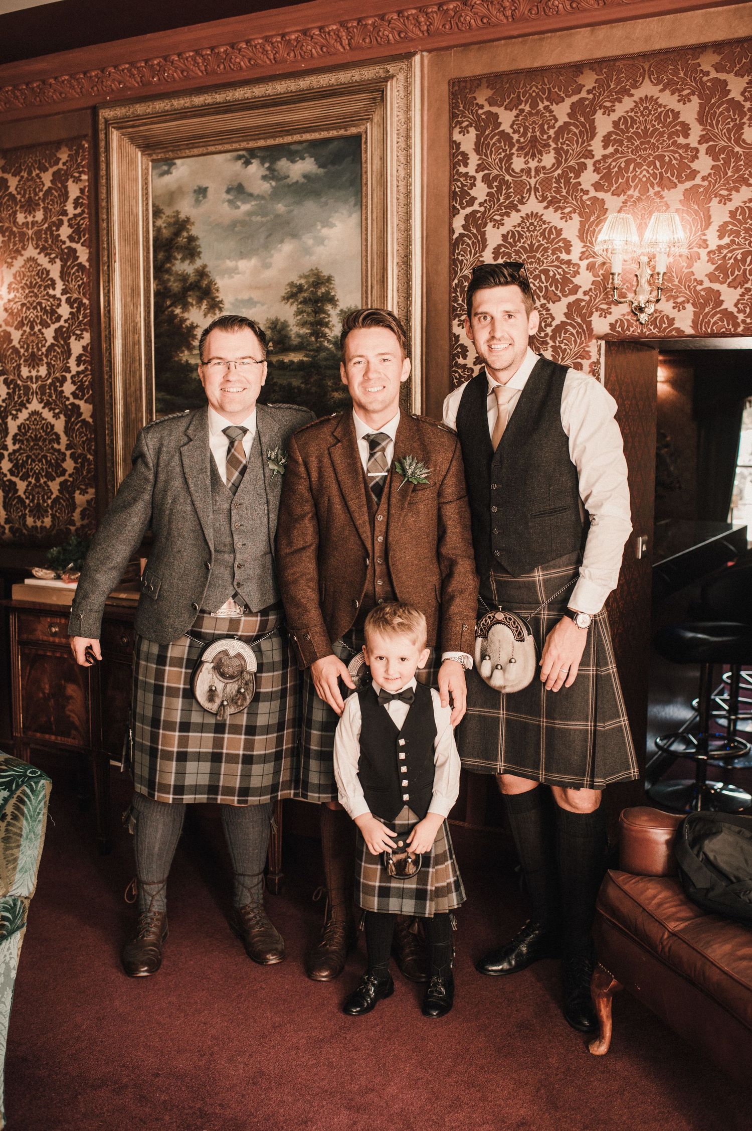 Traditional Scottish wedding attire with men in kilts posing in formal room.
