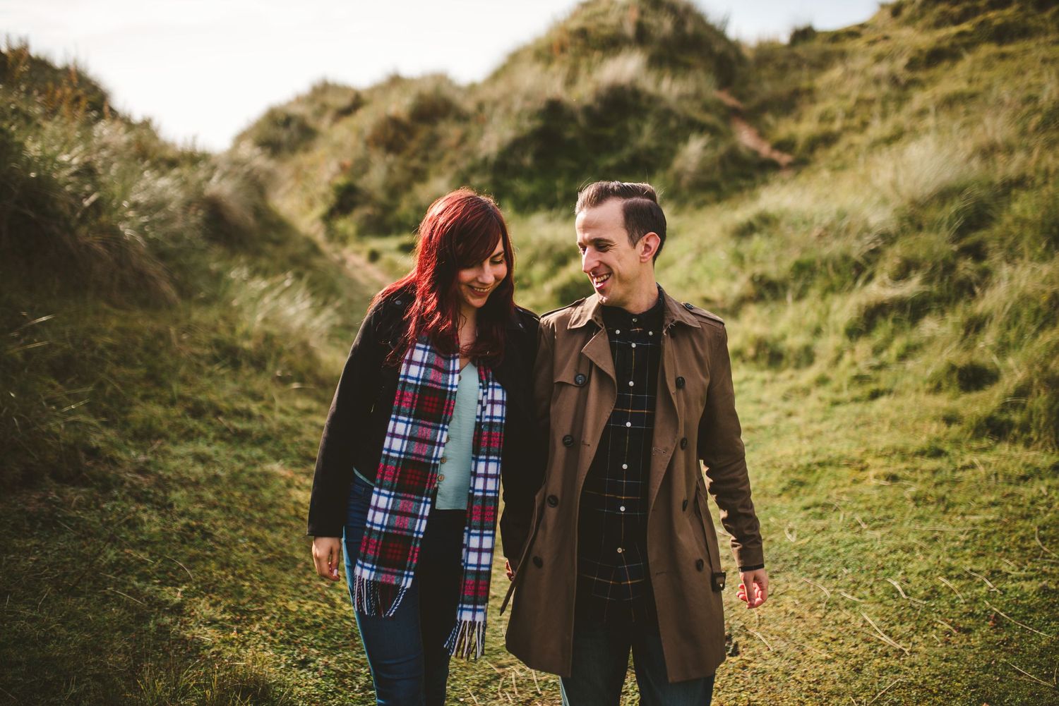 A couple sharing a warm moment while walking along grassy hills on an autumn day.