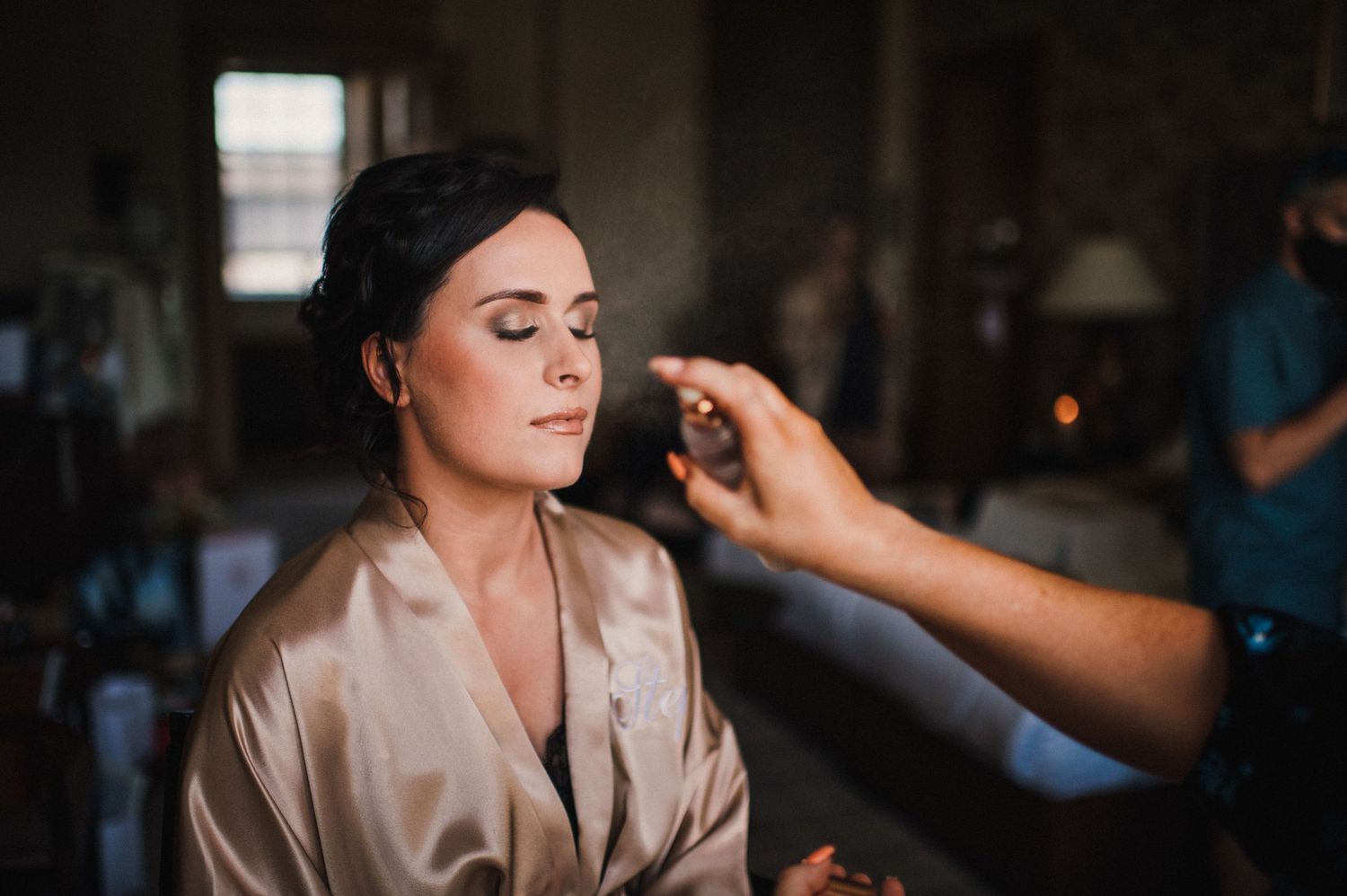 A makeup artist applies cosmetics on a client wearing a silk robe during wedding preparation.