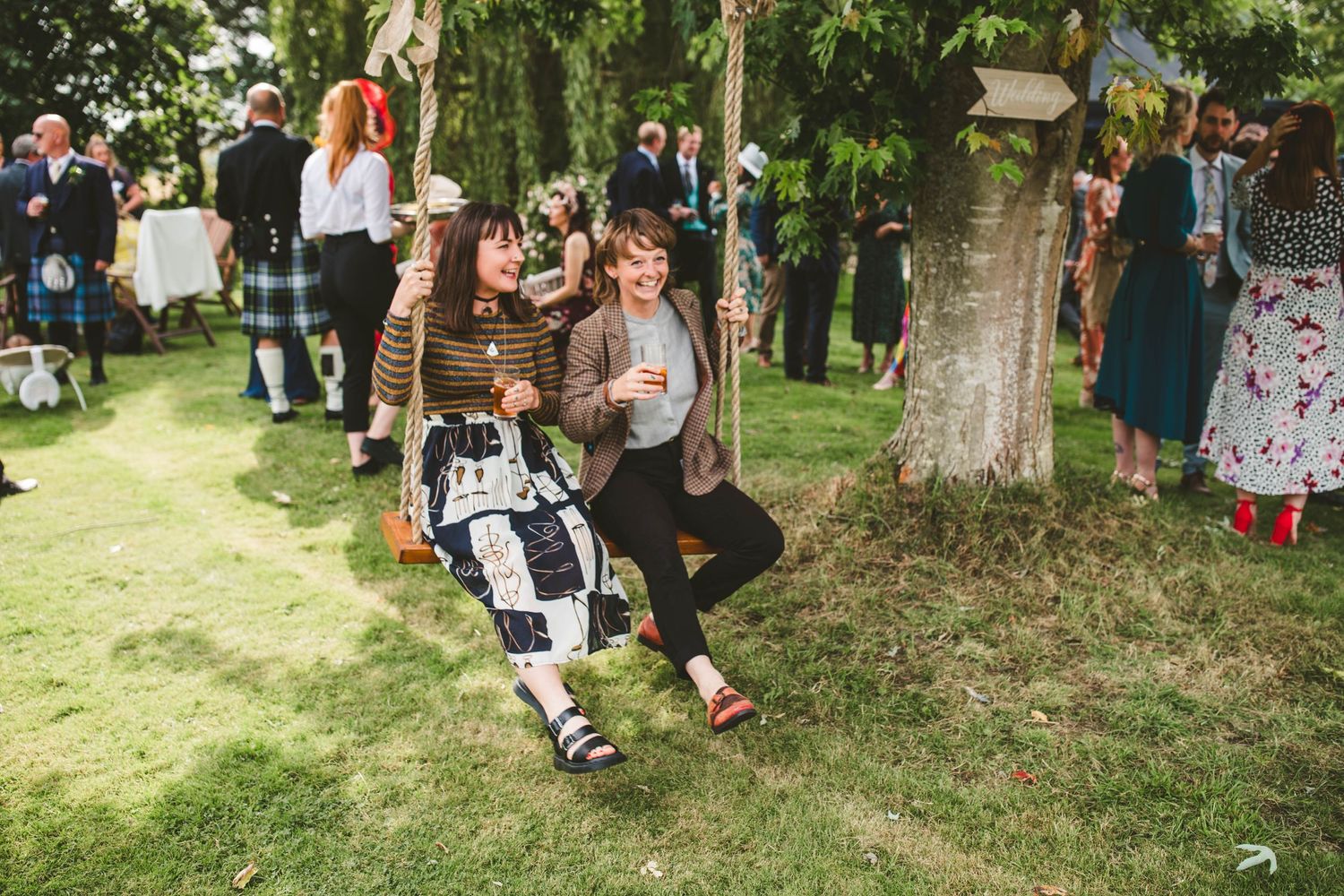 Child enjoys a swing while guests mingle at outdoor garden wedding.