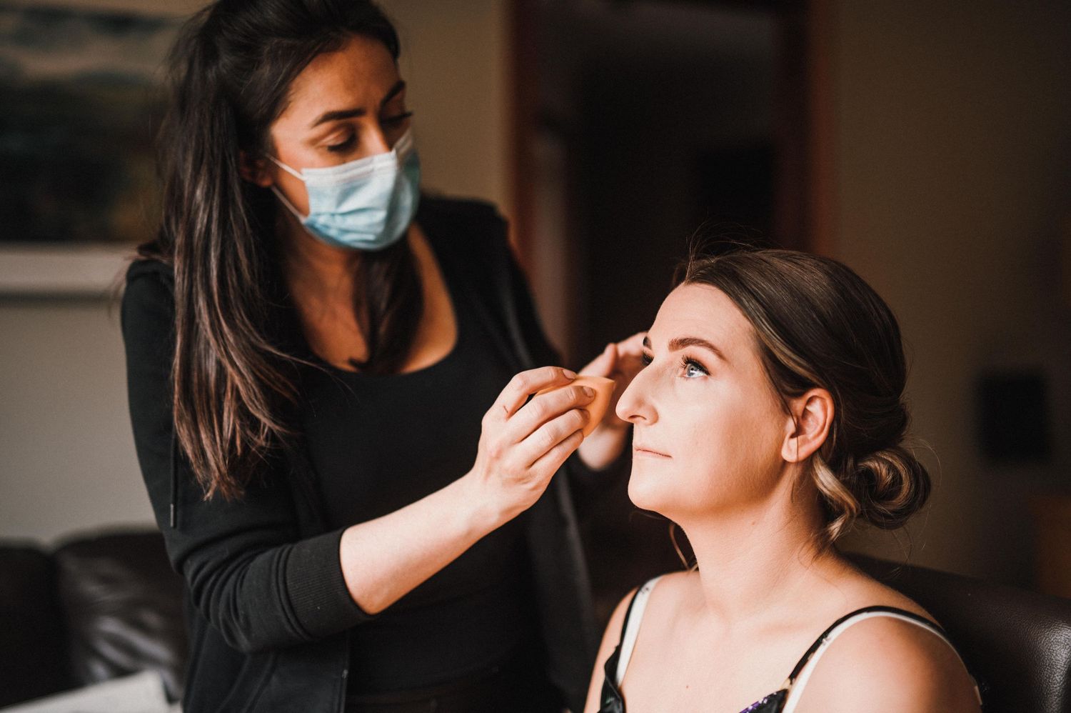 Professional makeup application session with artist wearing protective equipment.