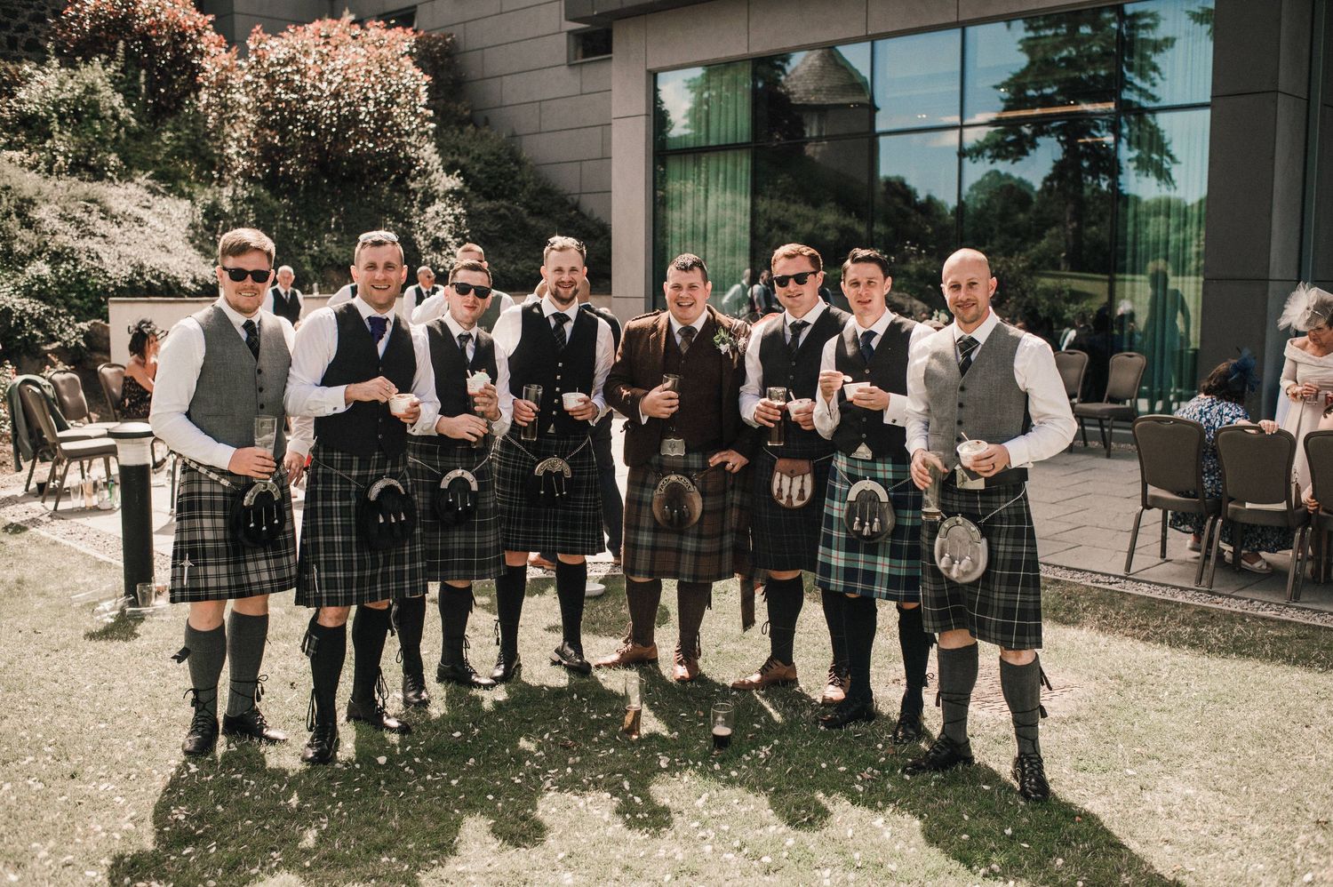 Men in traditional Scottish kilts and vests posing together at a wedding.
