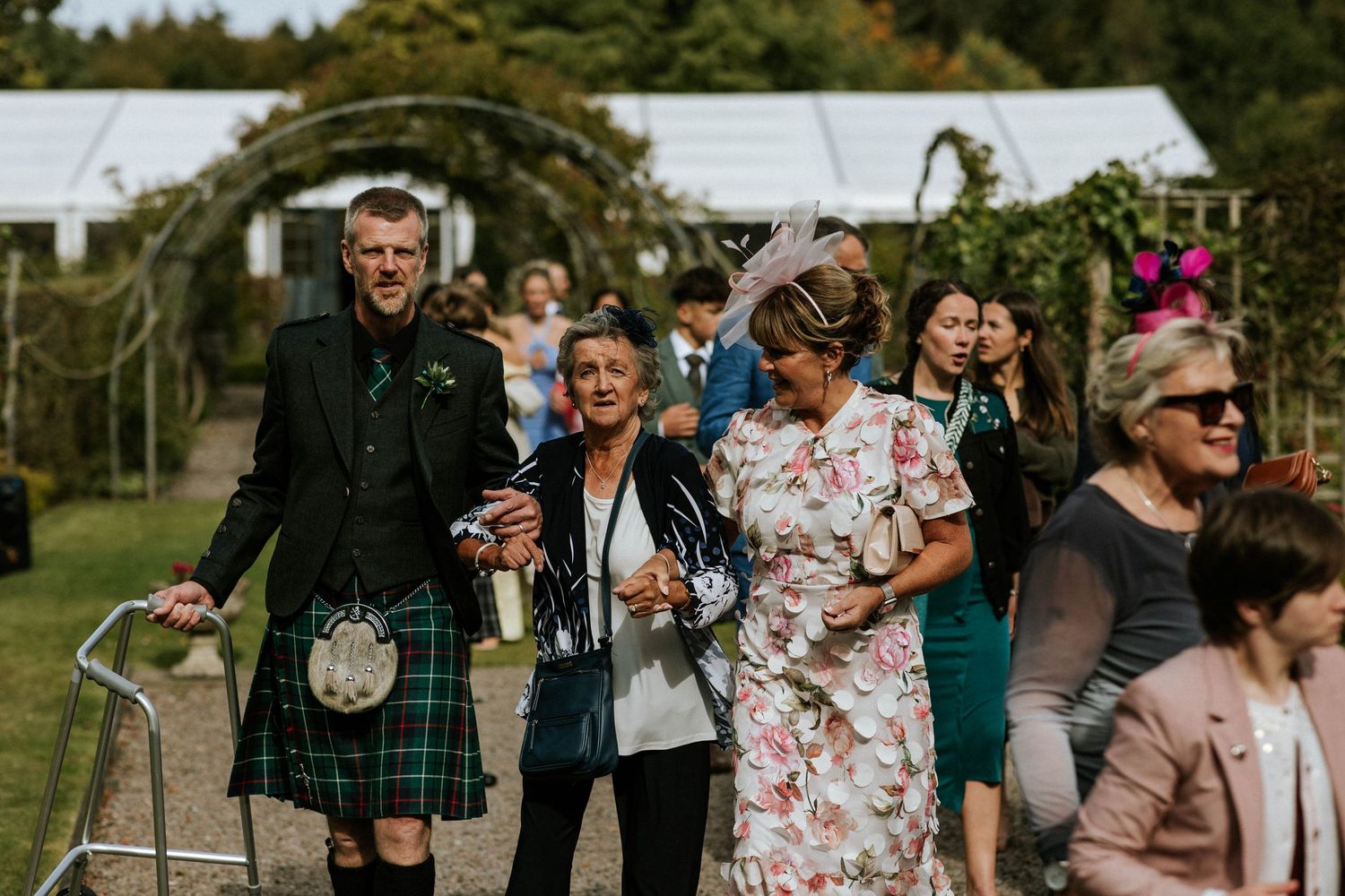 Wedding guests in summer attire gather outdoors during a garden celebration.