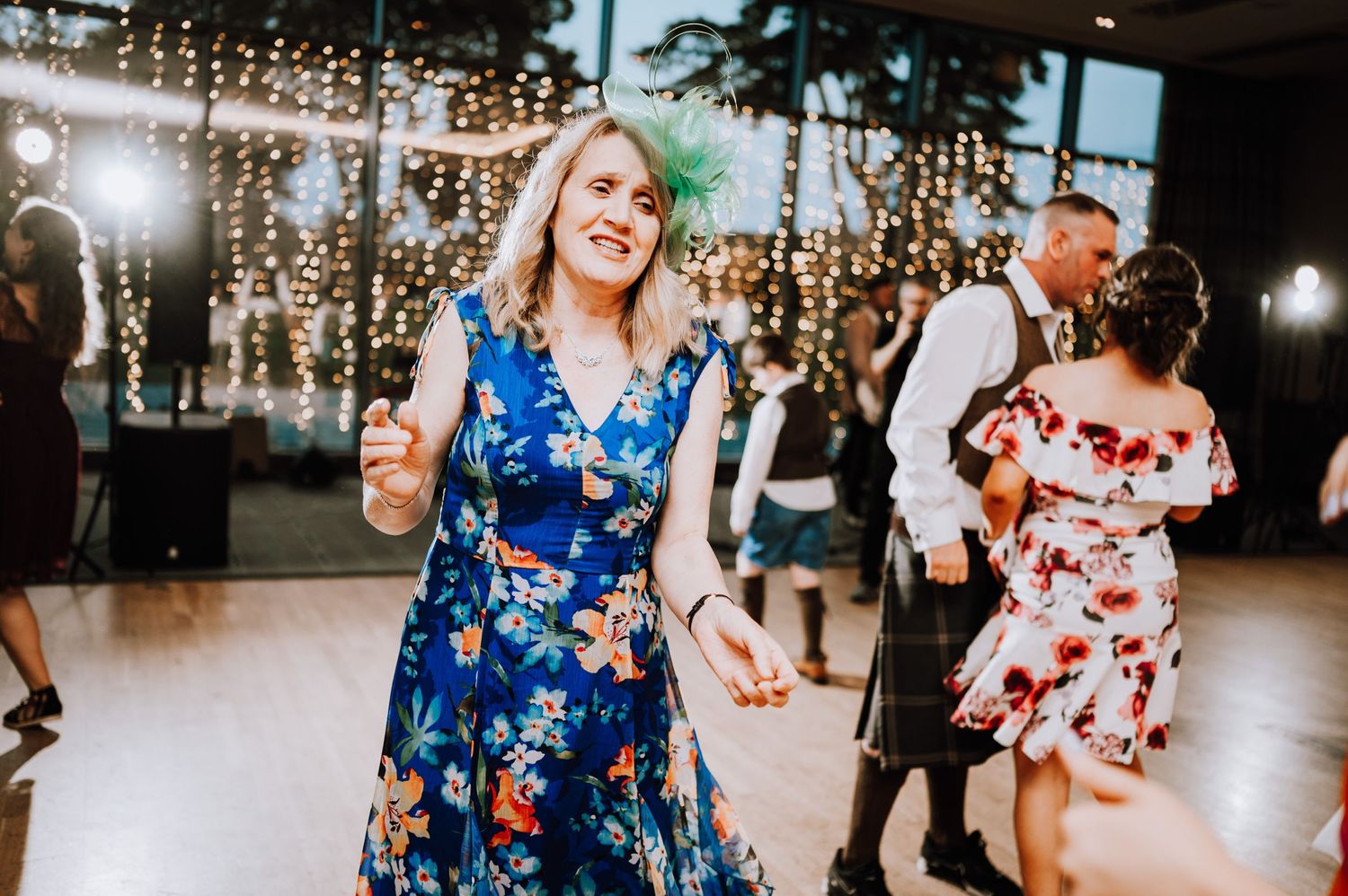 A person in a blue floral dress dances joyfully at a wedding reception.