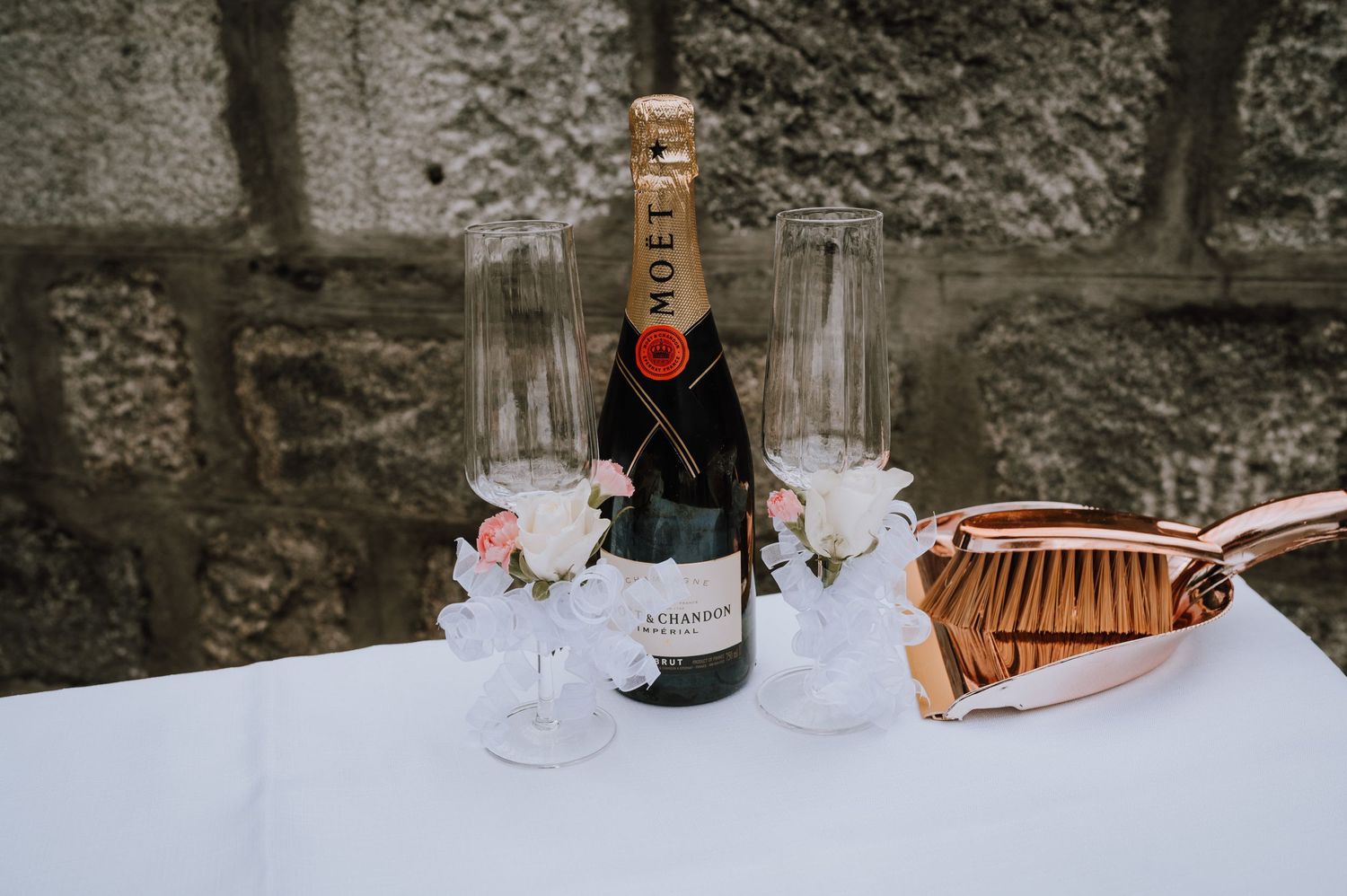 Moet champagne bottle with glasses and copper decor on white tablecloth against stone wall.