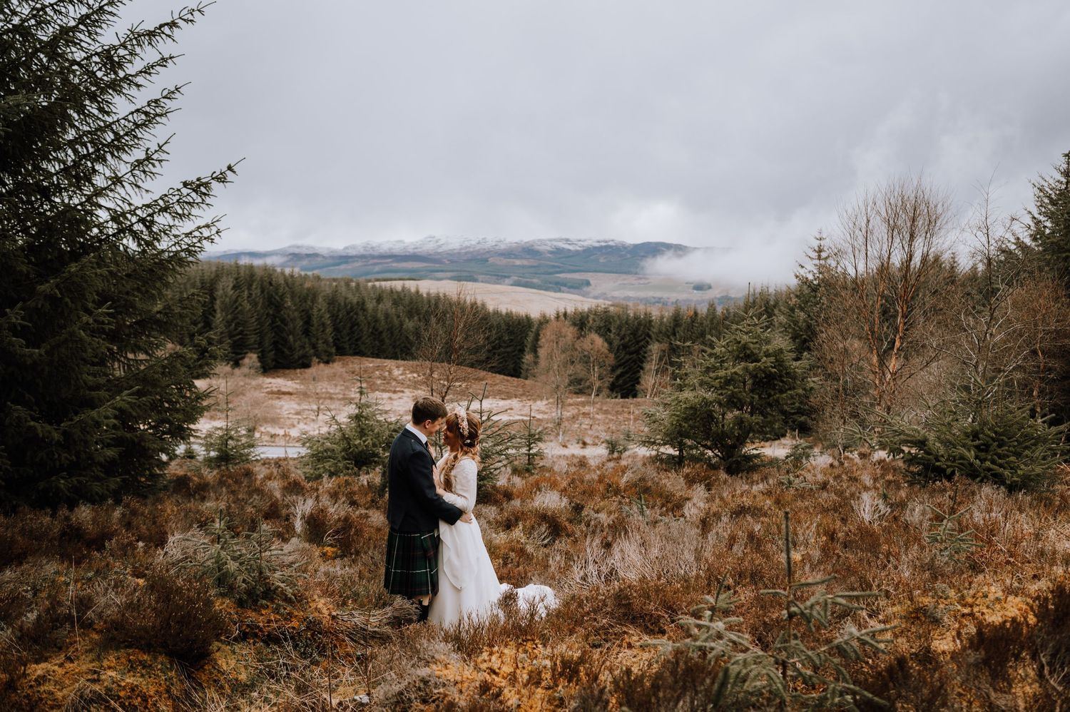 Wedding couple embracing in mountainous Scottish landscape with dramatic views and autumn colors.