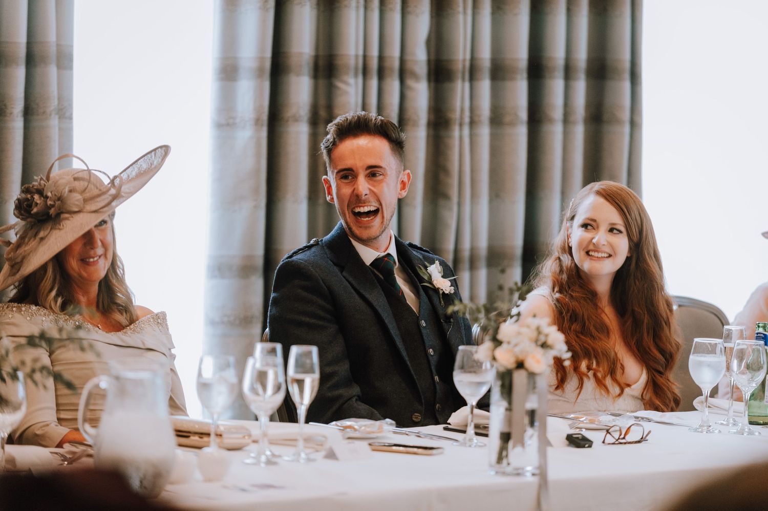 Reception guests react with laughter during wedding speeches at an elegant venue.