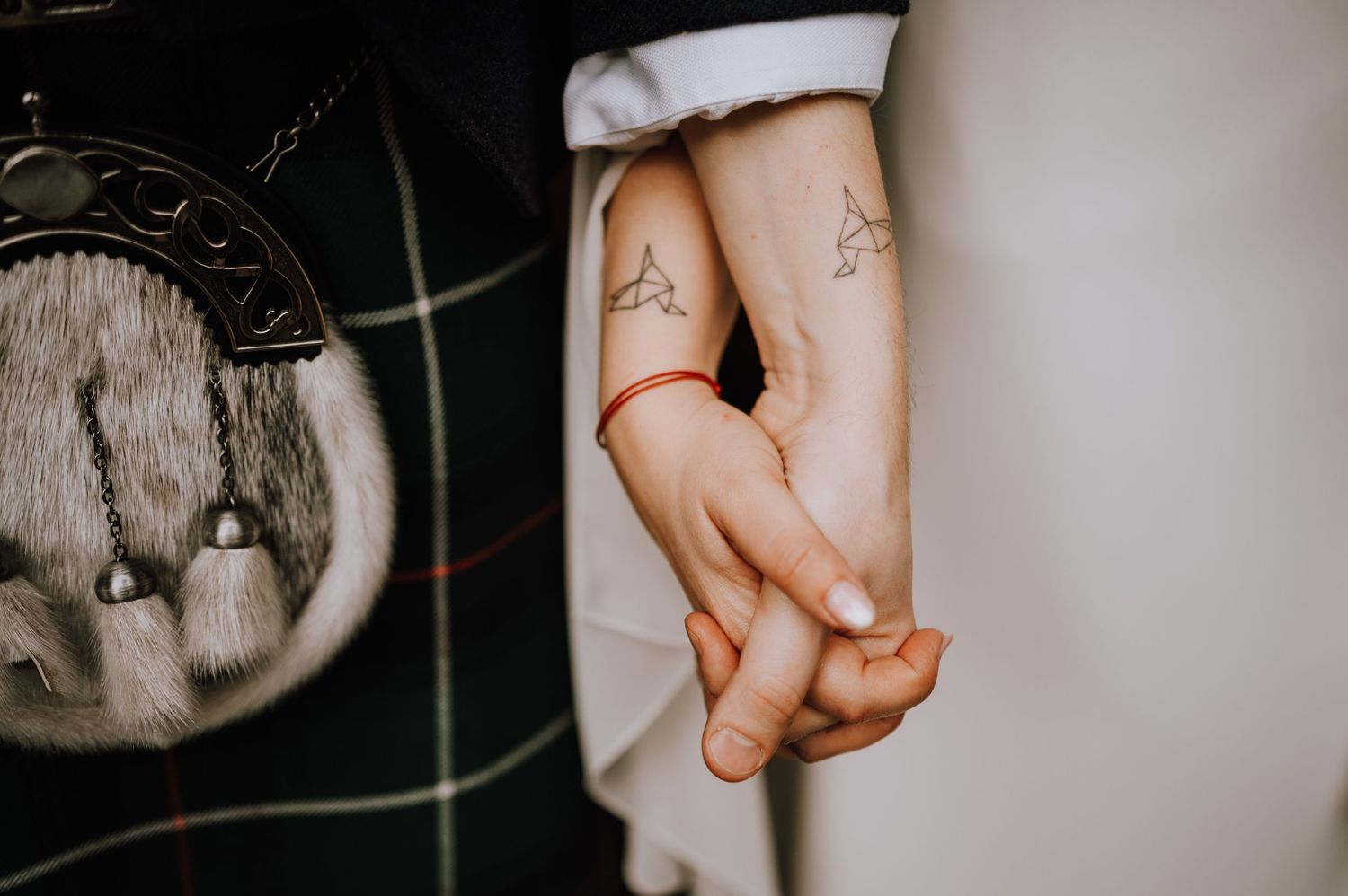 Close-up of held hands against plaid fabric showing delicate tattoos.