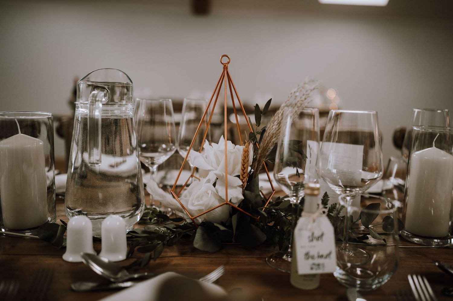 Moody reception table setting with glass centerpieces, candles, and floral arrangements.