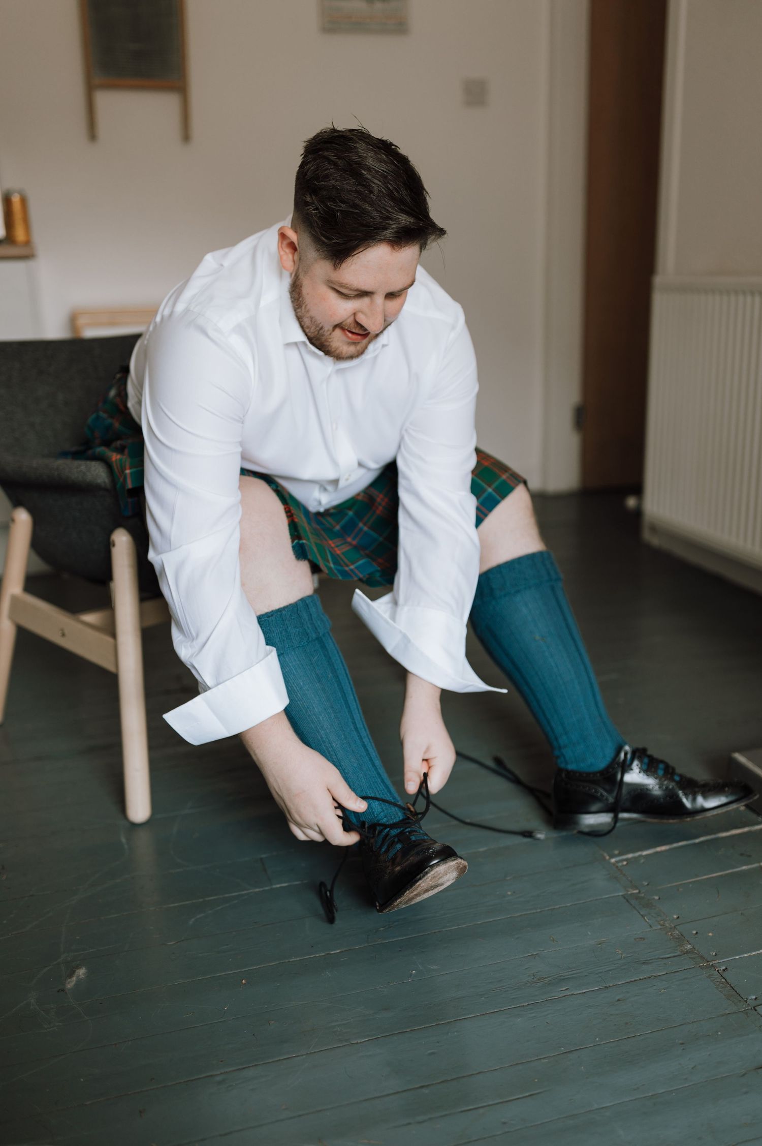 Person in formal white shirt and kilt adjusting dark dress socks.