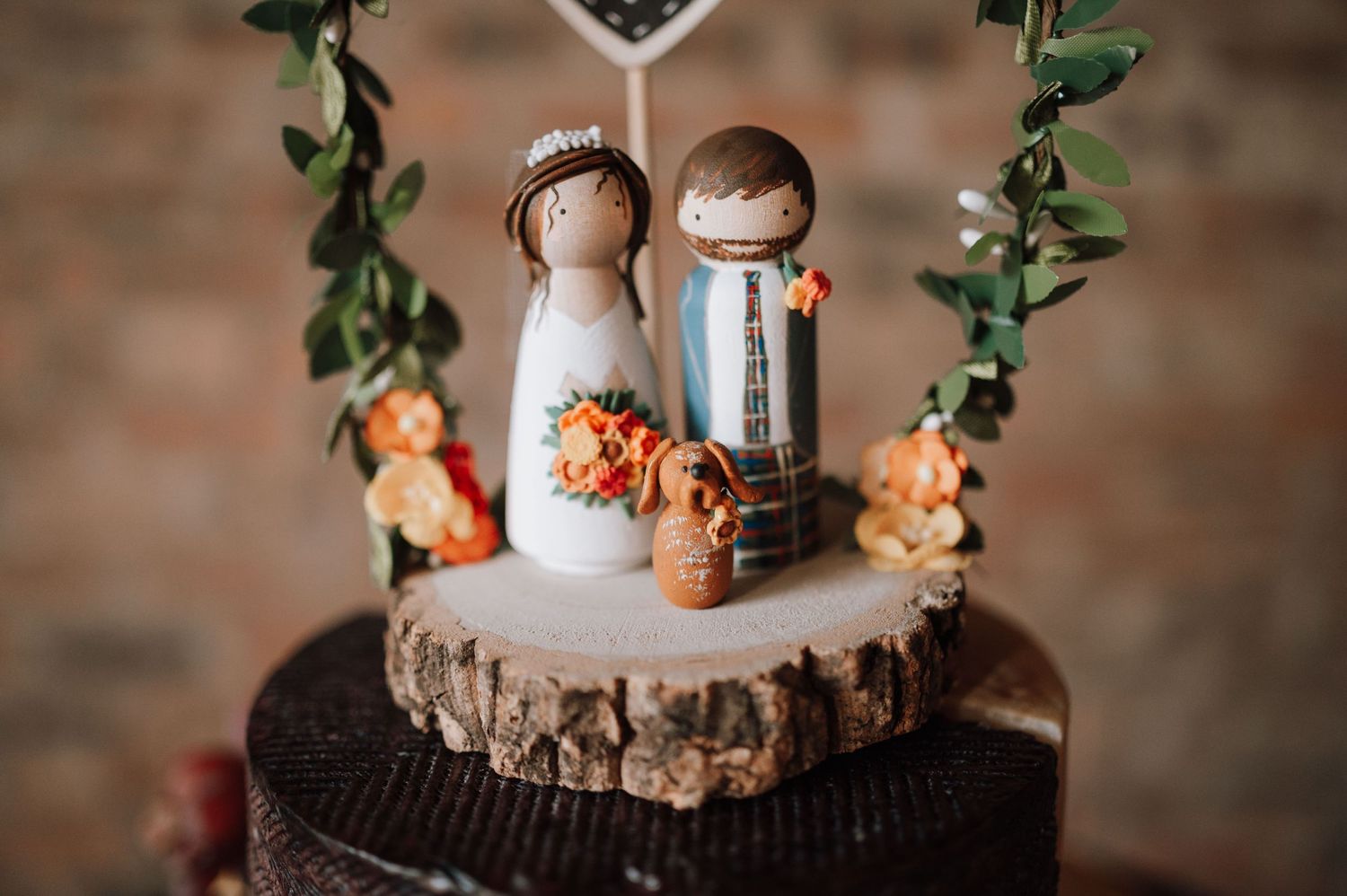 Wooden cake topper figures with floral decorations on rustic tree slice stand.