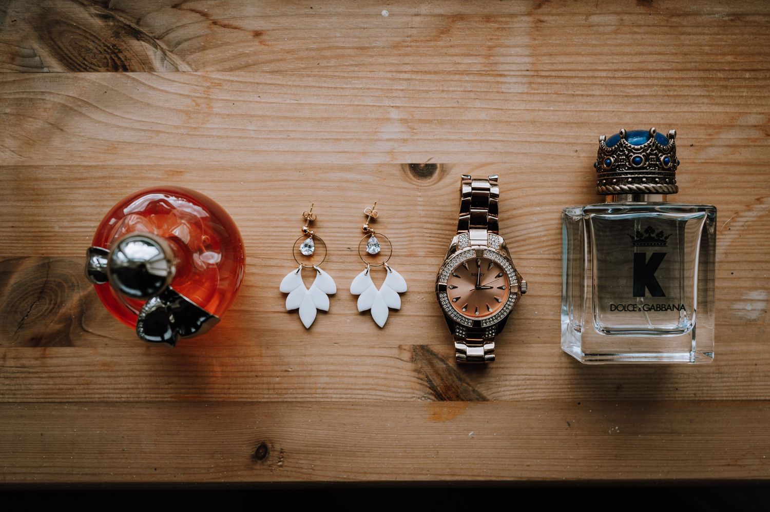 Wedding accessories including perfume, watch, earrings, and jewelry laid out on wooden surface.