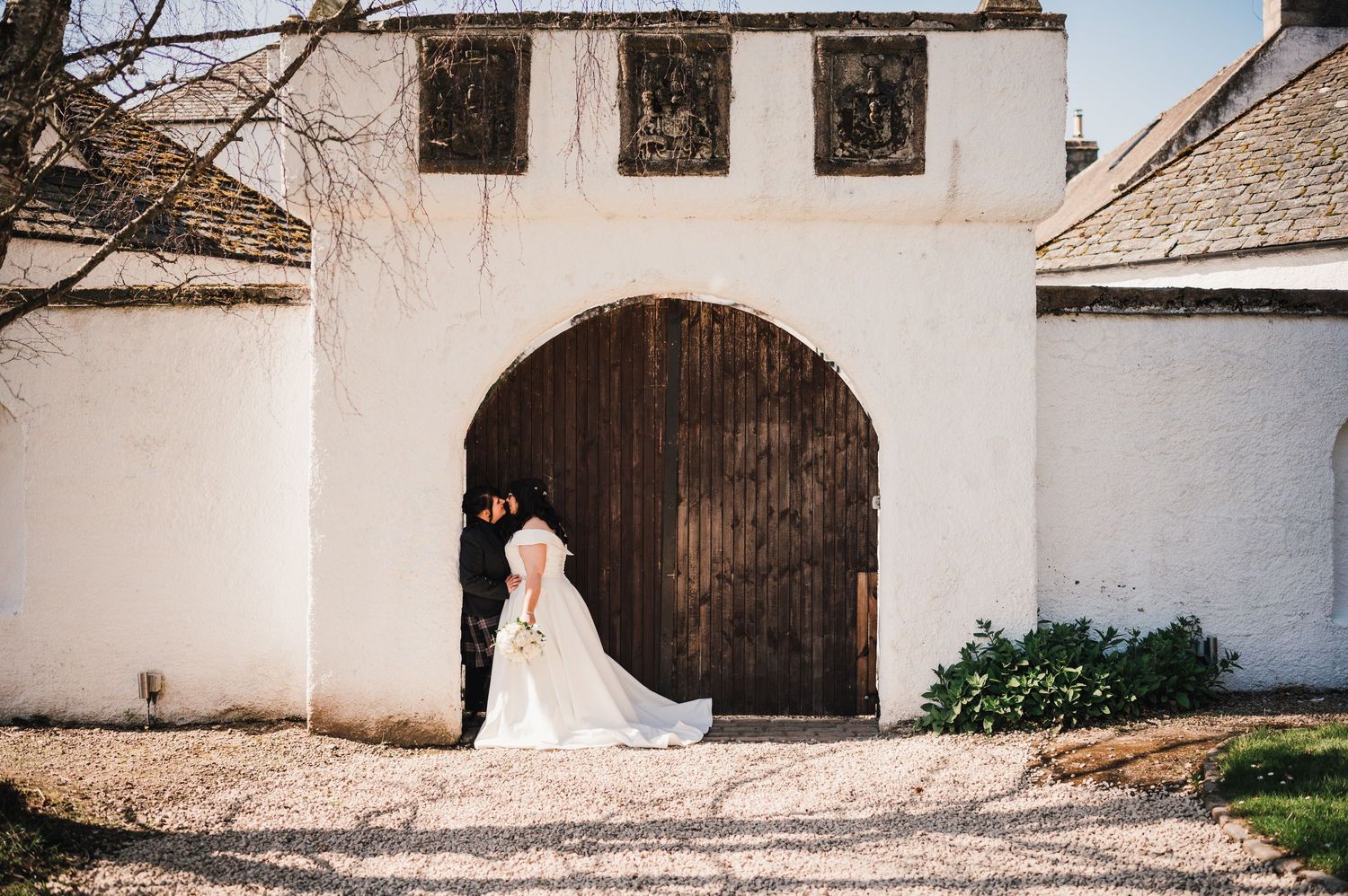 Logie House Wedding Photography. A white wedding dress train flows across the ground in front of a rustic arched doorway.