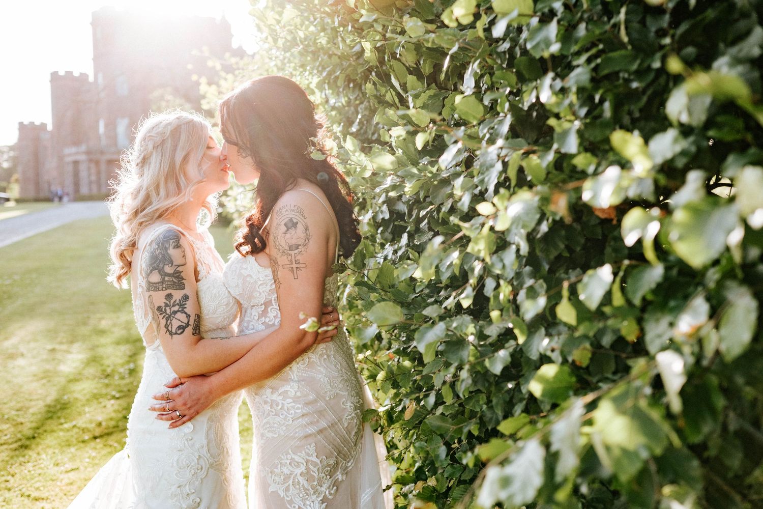 Aberdeen Wedding Photography. Two brides share an intimate moment against a backdrop of greenery and castle walls at sunset.