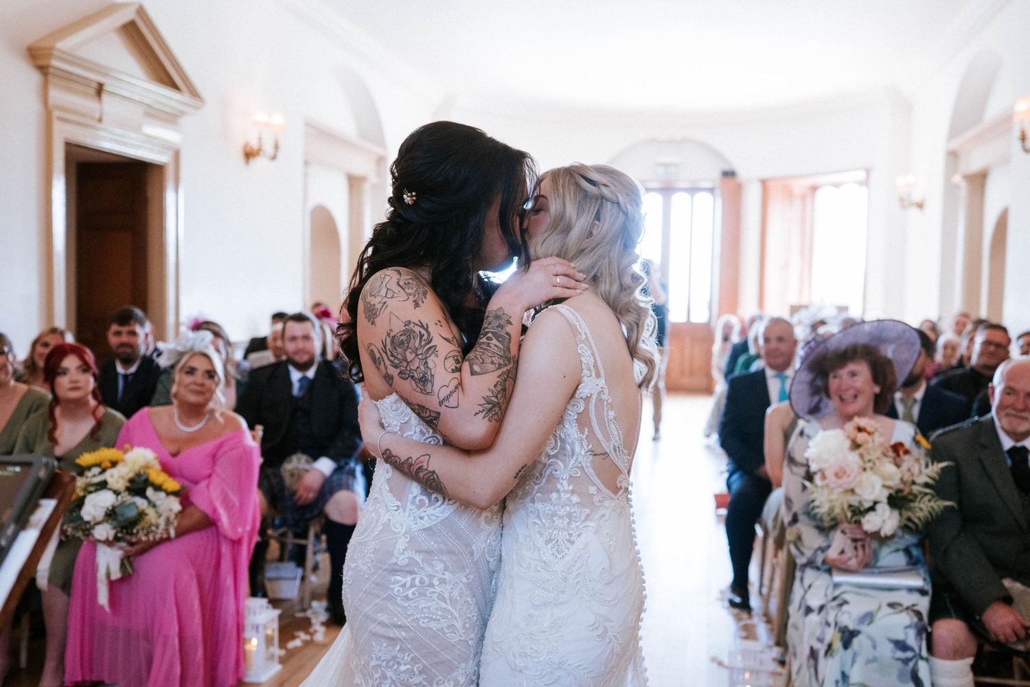 Intimate wedding ceremony moment captured in bright white venue with guests looking on.